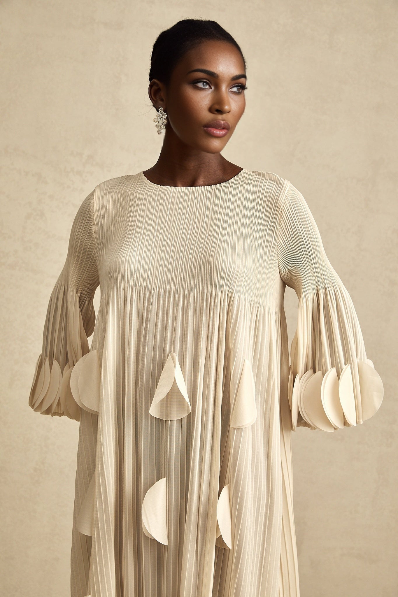 Woman wearing a light colored midi dress with three dimensional pleated petals flowing from waist to hem