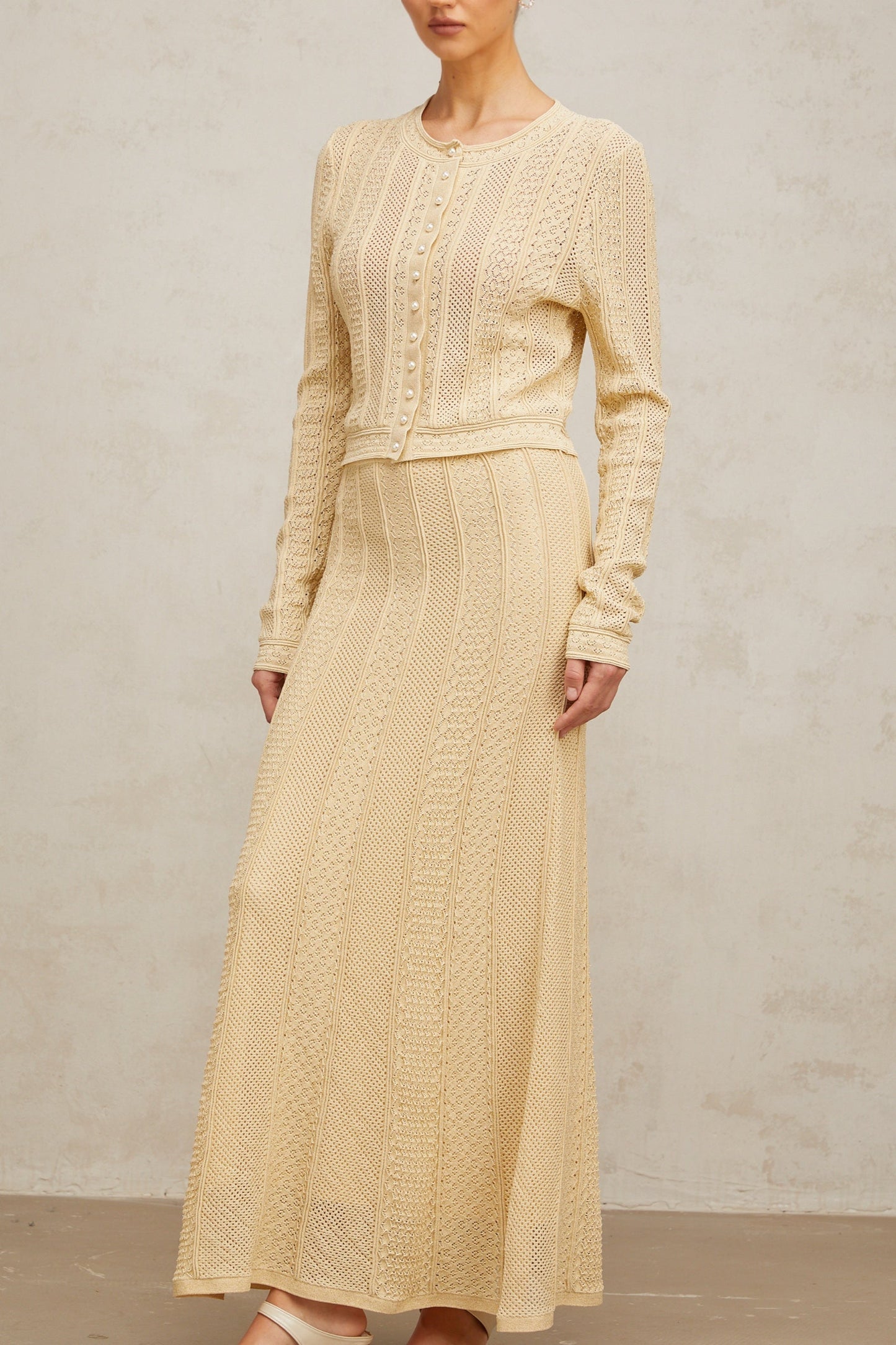 Woman wearing a light colored pointelle knit cardigan and matching skirt set posing against a neutral background