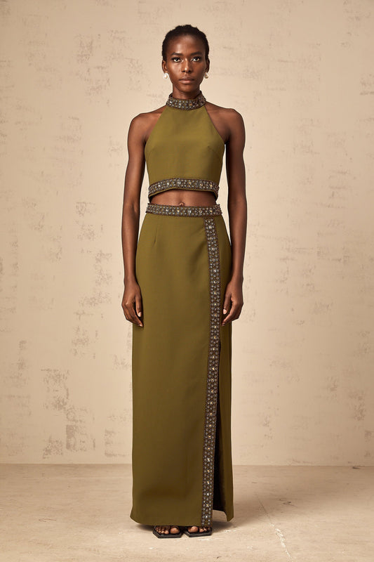 Woman wearing a light green twopiece outfit consisting of a sleeveless top and skirt with daisyinspired beaded trim along the edges