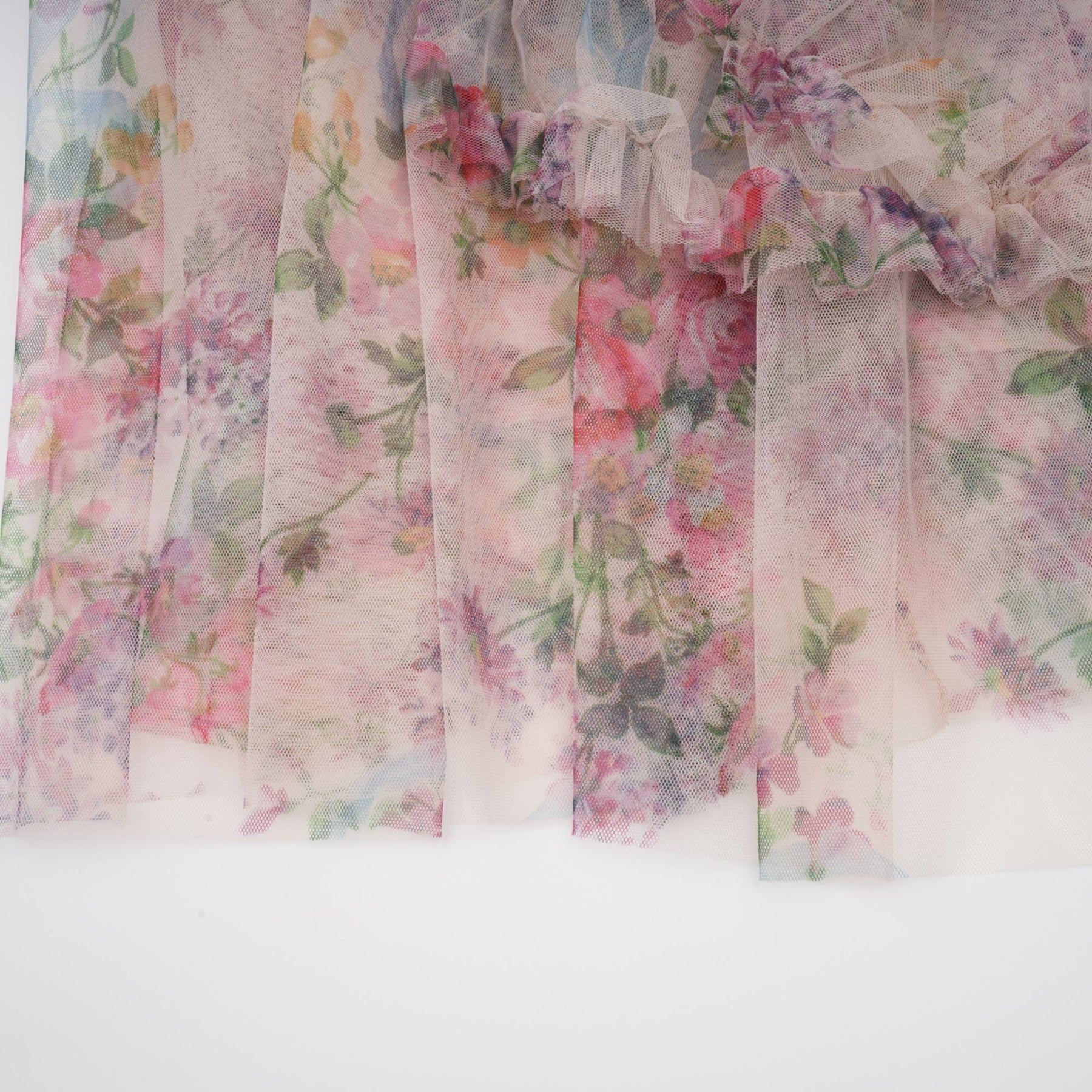 Woman wearing a lightcolored floral midi dress with ruffled details and tulle overlay standing against a plain background