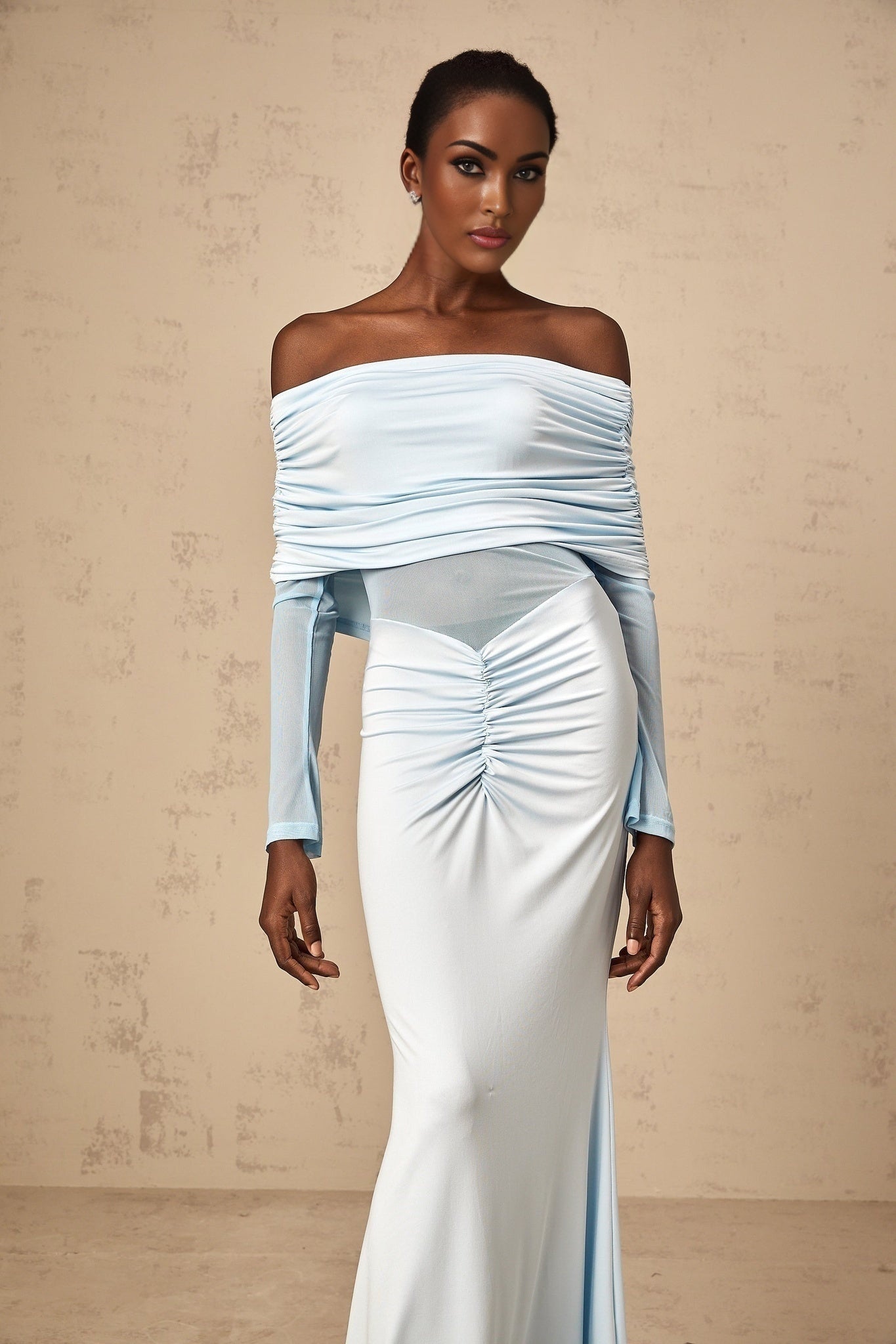 Woman wearing a long blue offshoulder dress with ruched details and flowing maxi length skirt