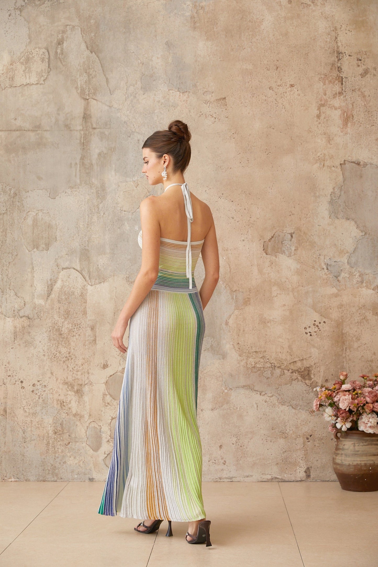 Woman wearing a long metallic knit maxi dress with backless design standing in elegant pose