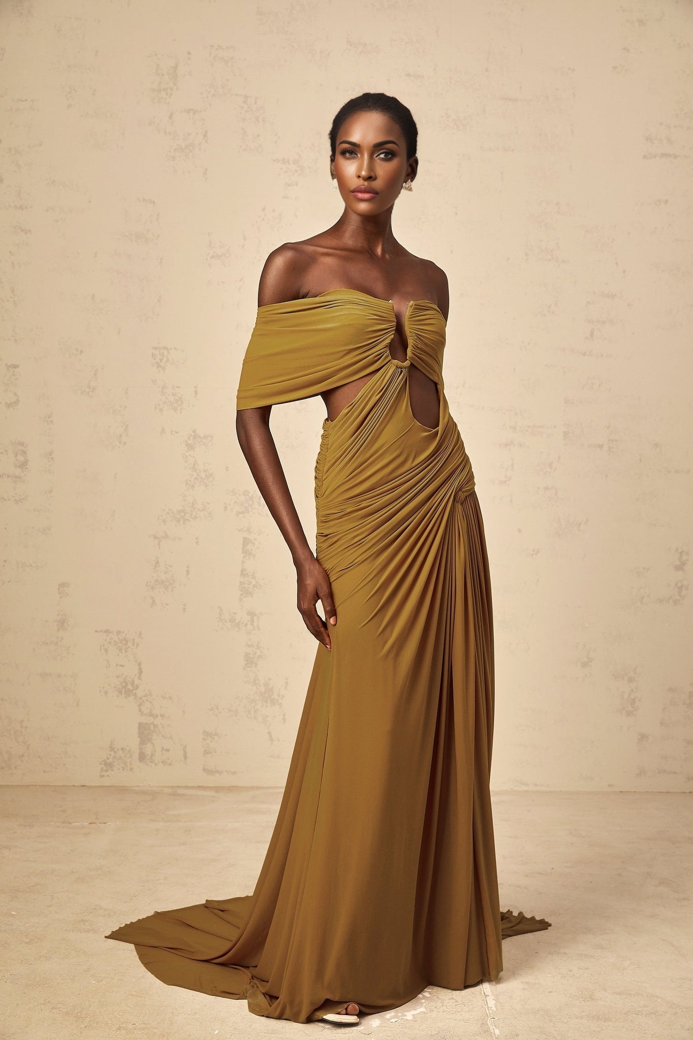 Woman wearing a long ocher colored dress with off shoulder design ruched details and cut out elements