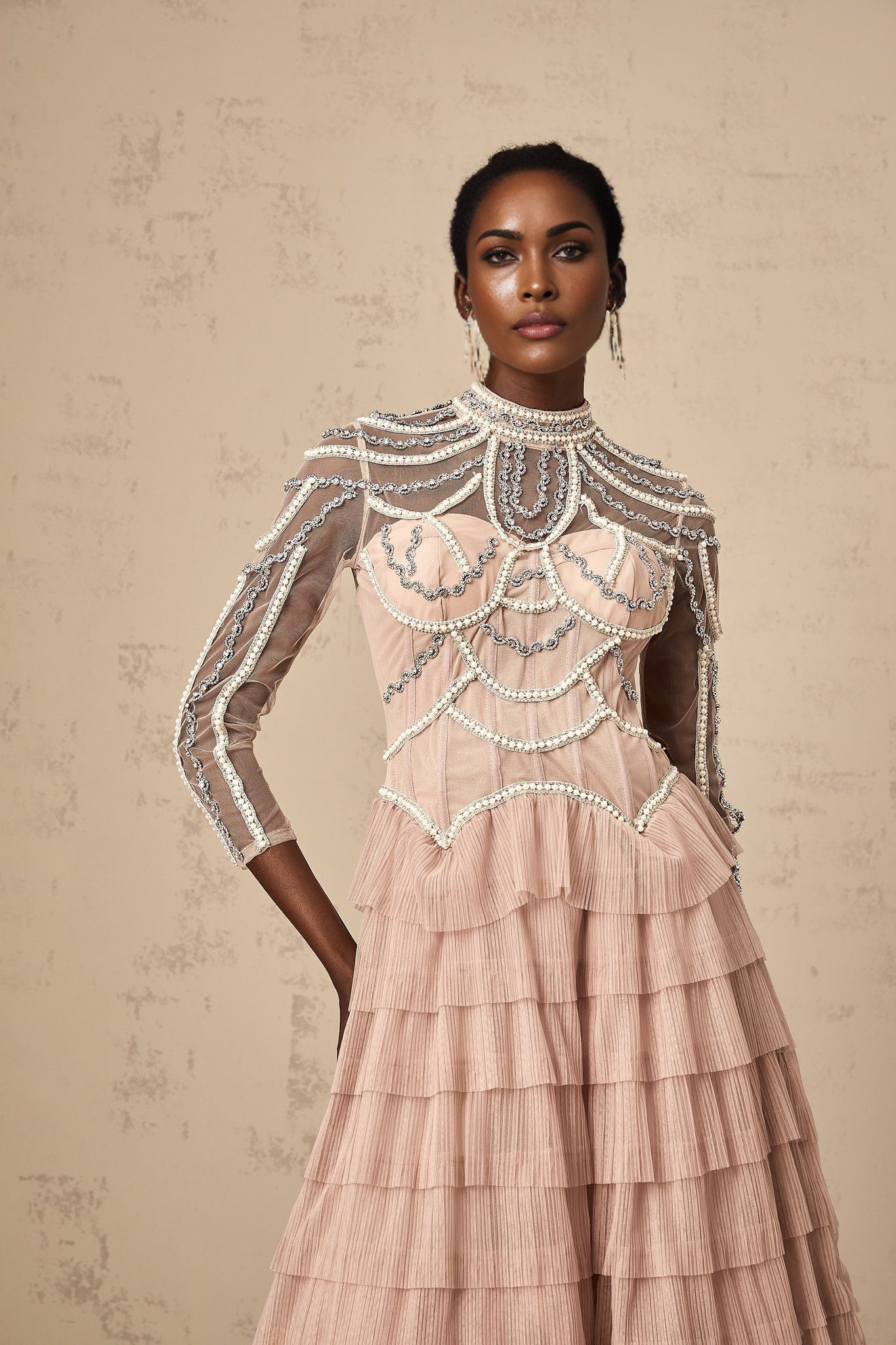 Woman wearing a long pink gown with tiered layers and beaded details flowing sheer fabric with a soft romantic look