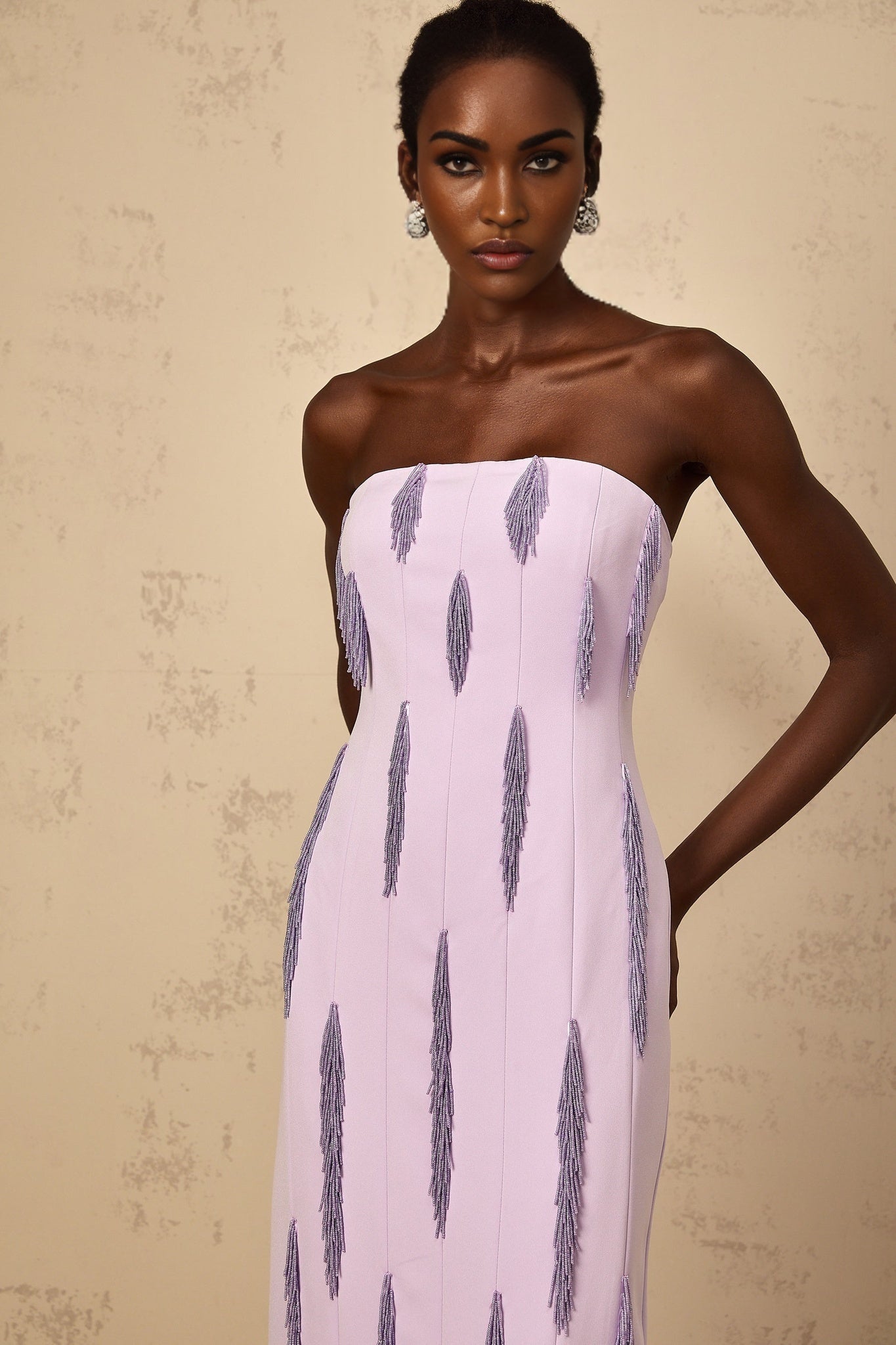 Woman wearing a long purple maxi dress with beaded fringe details and spaghetti straps standing in a relaxed pose