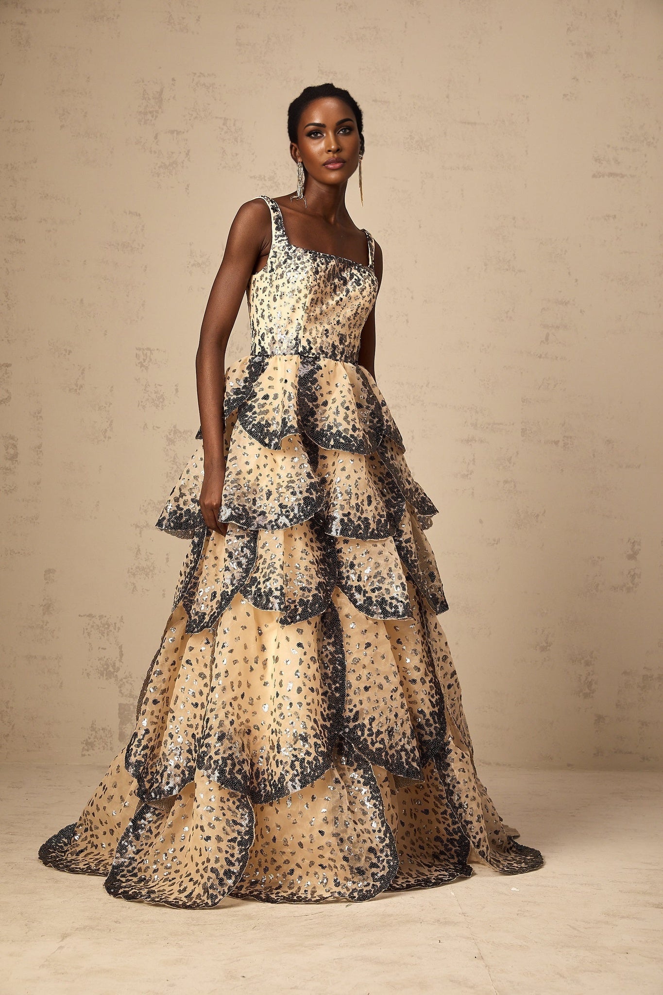 Woman wearing a long tiered maxi dress with sequined petal details and a flowing silhouette