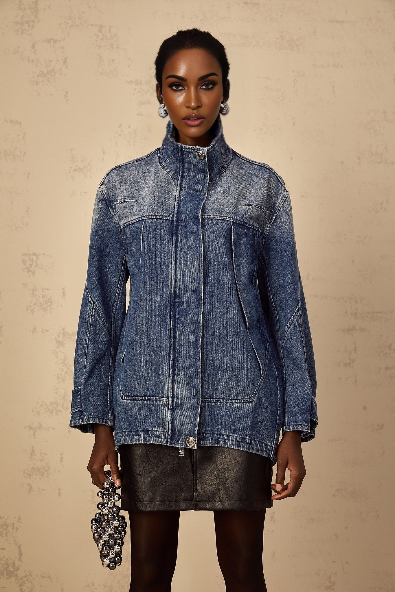 Woman wearing a loose fitting blue denim jacket with patchwork design against a plain background