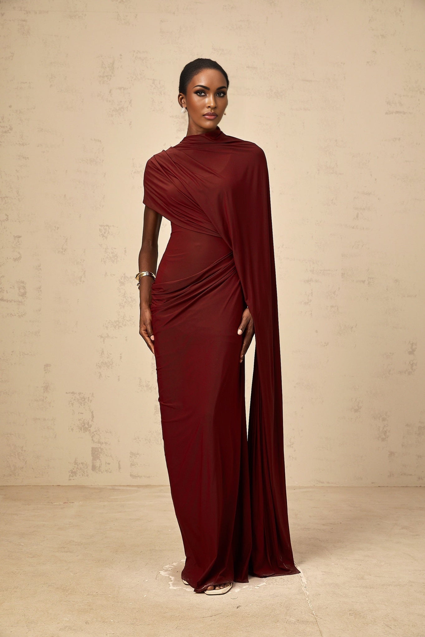 Woman wearing a matching asymmetrical draped cape and dress set in black fabric with flowing lines and elegant draping