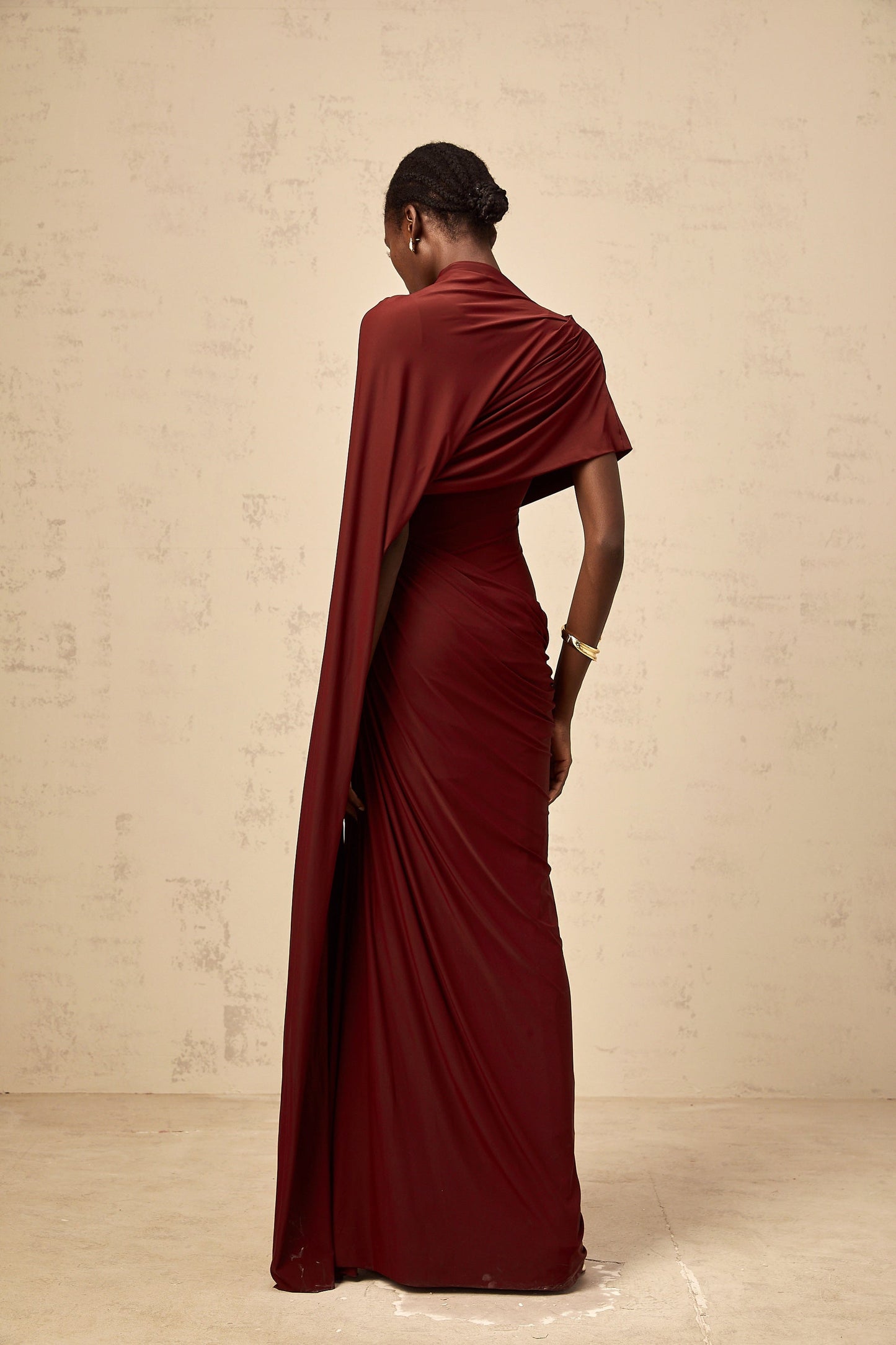 Woman wearing a matching set consisting of an asymmetrical draped cape and dress in a flowing fabric The cape drapes elegantly over one shoulder while the dress hugs the body