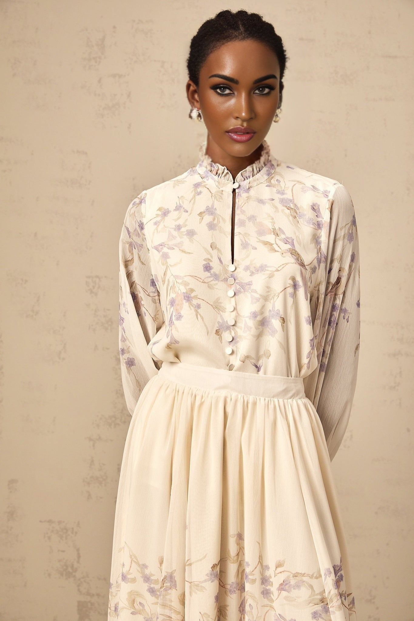 Woman wearing a matching set with a frilled shirt and skirt in wisteria print purple floral pattern on light background