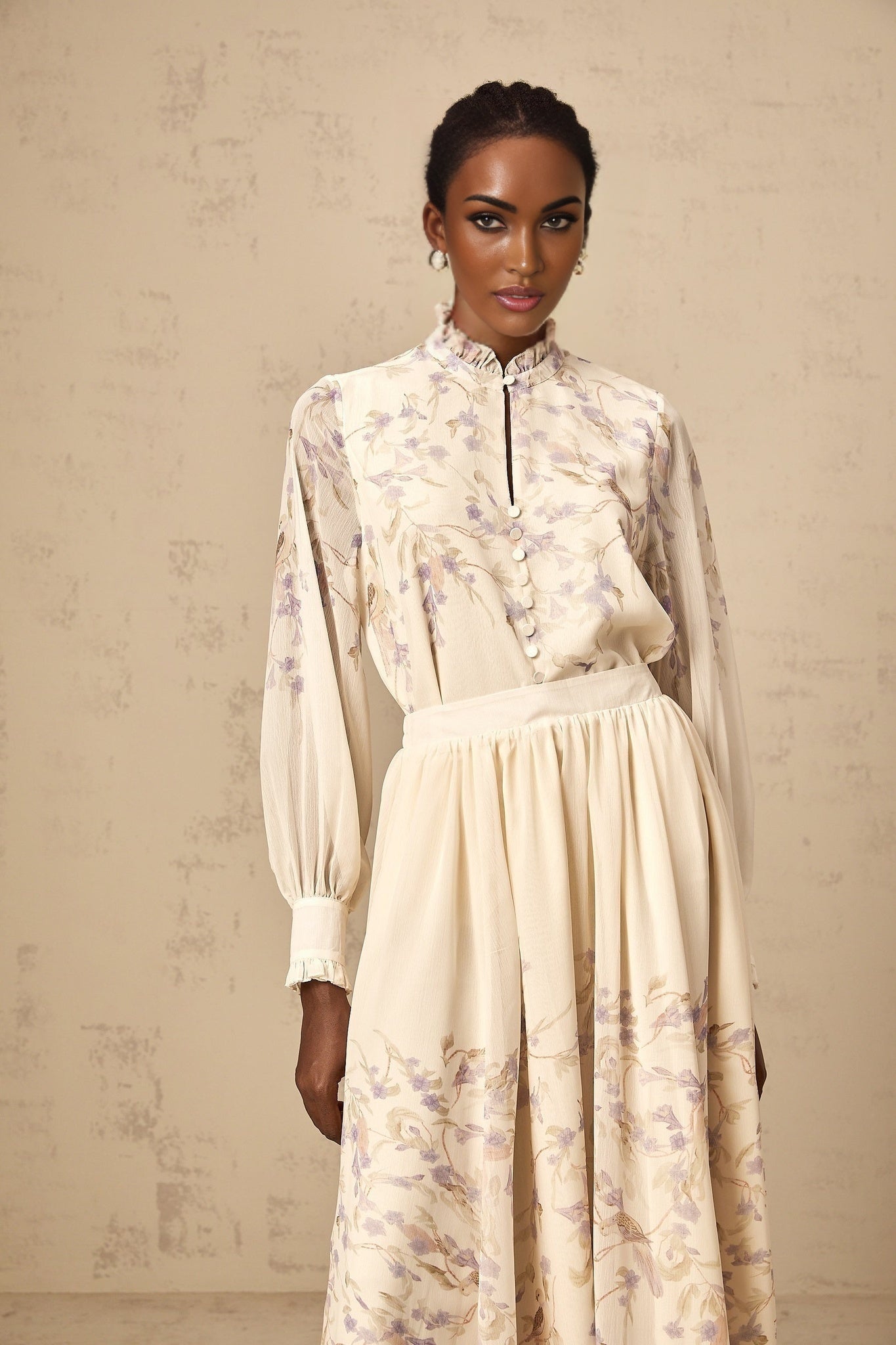 Woman wearing a matching shirt and skirt set with frilled details and wisteria floral print in light colors