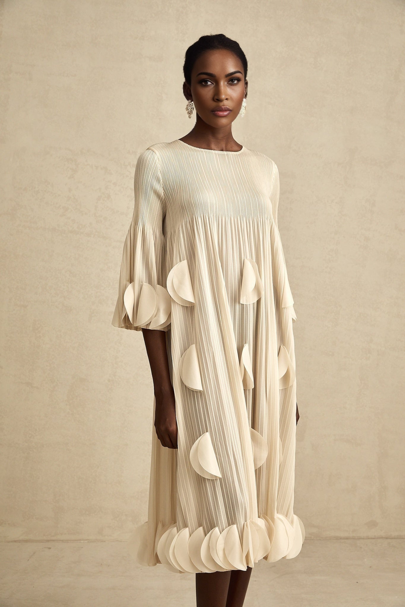 Woman wearing a midi length dress with three dimensional petal pleats in a flowing silhouette