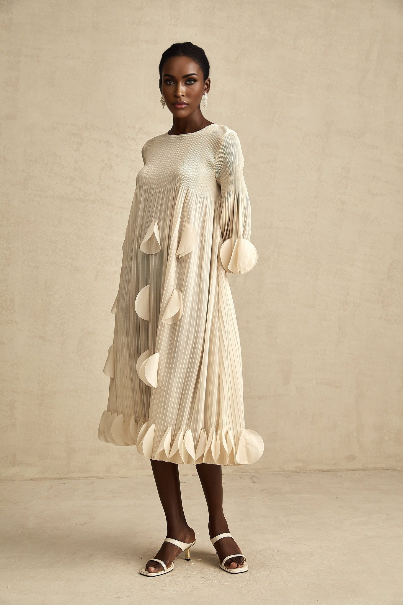 Woman wearing a navy blue midi dress with 3d petal pleated details throughout the bodice and skirt