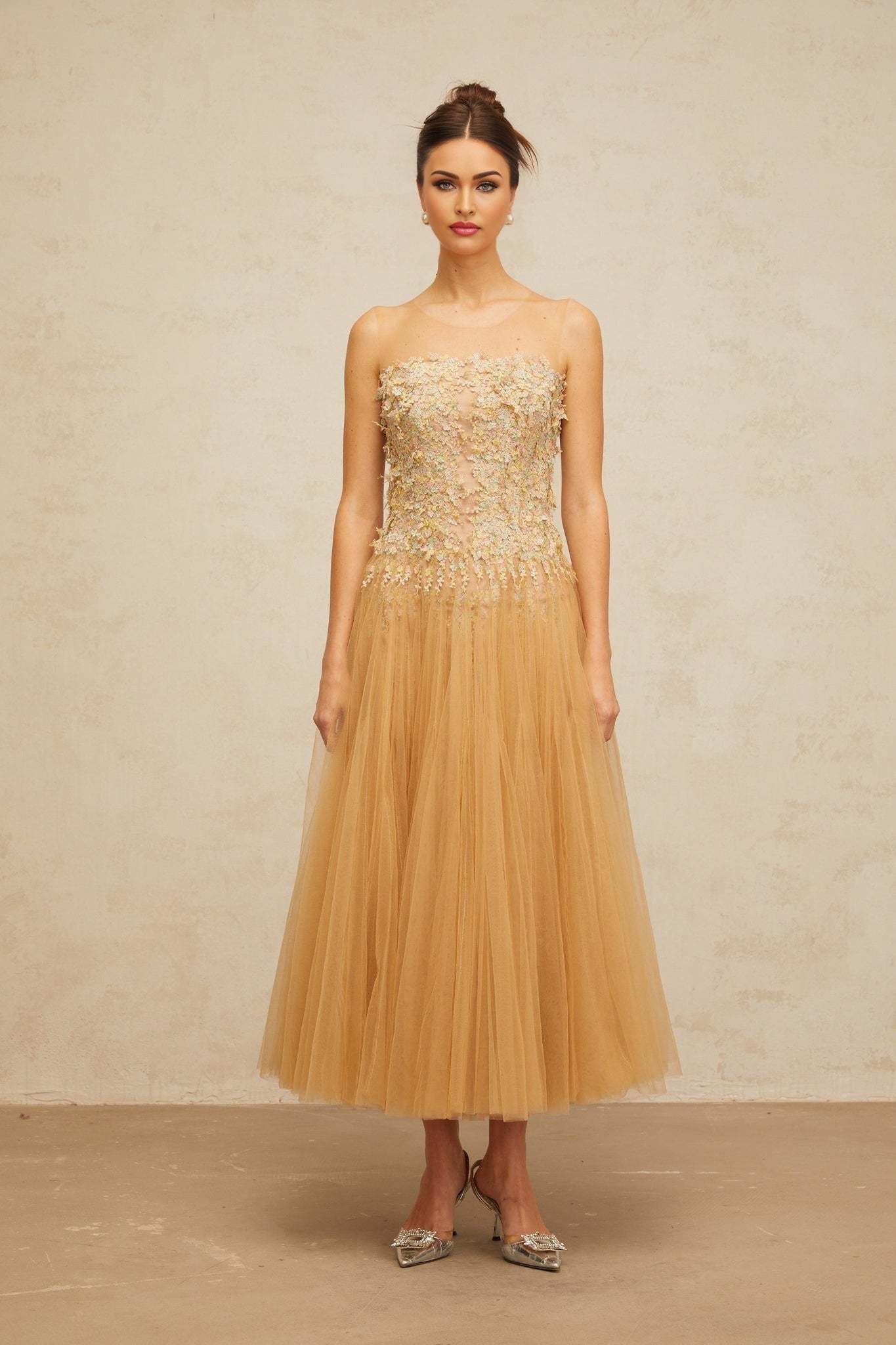 Woman wearing a neutral colored knee length dress with pleated tulle and sequin embellishments