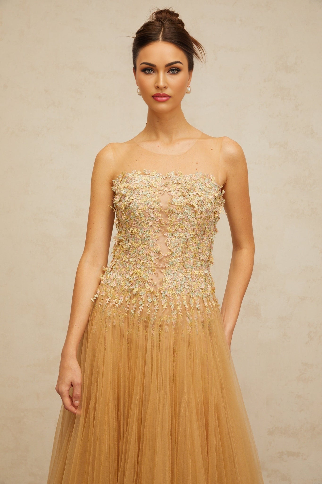 Woman wearing a neutral colored knee length dress with pleated tulle fabric and sequin embellishments