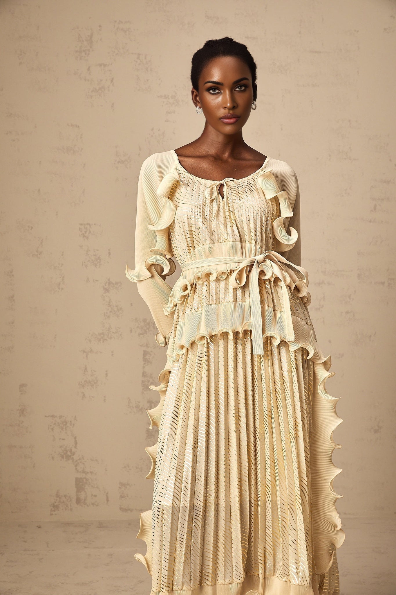 Woman wearing a neutral colored midi dress with gilded ruffles and a ruched bodice