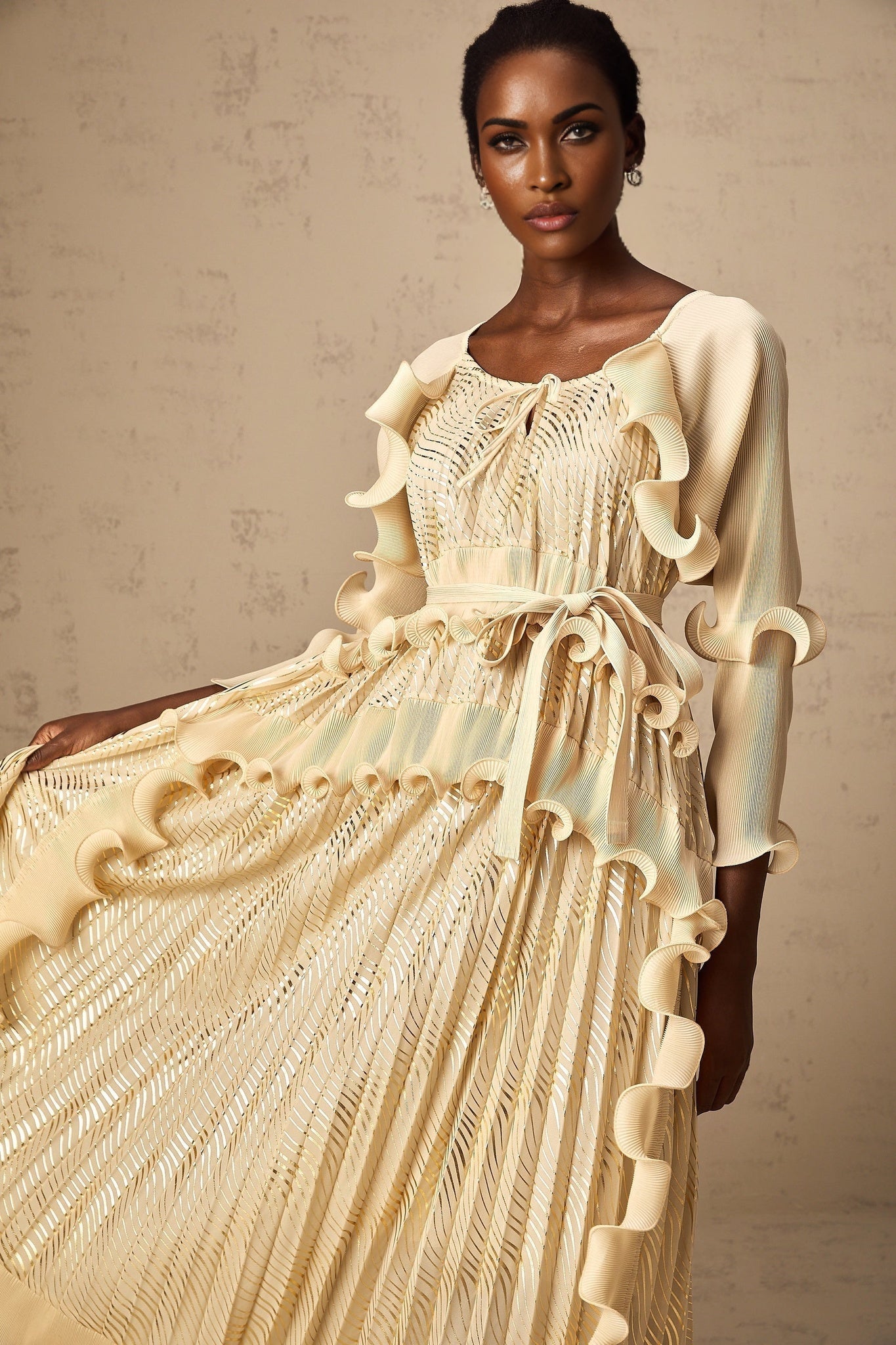 Woman wearing a neutral colored midi dress with gilded ruffles and ruffle details