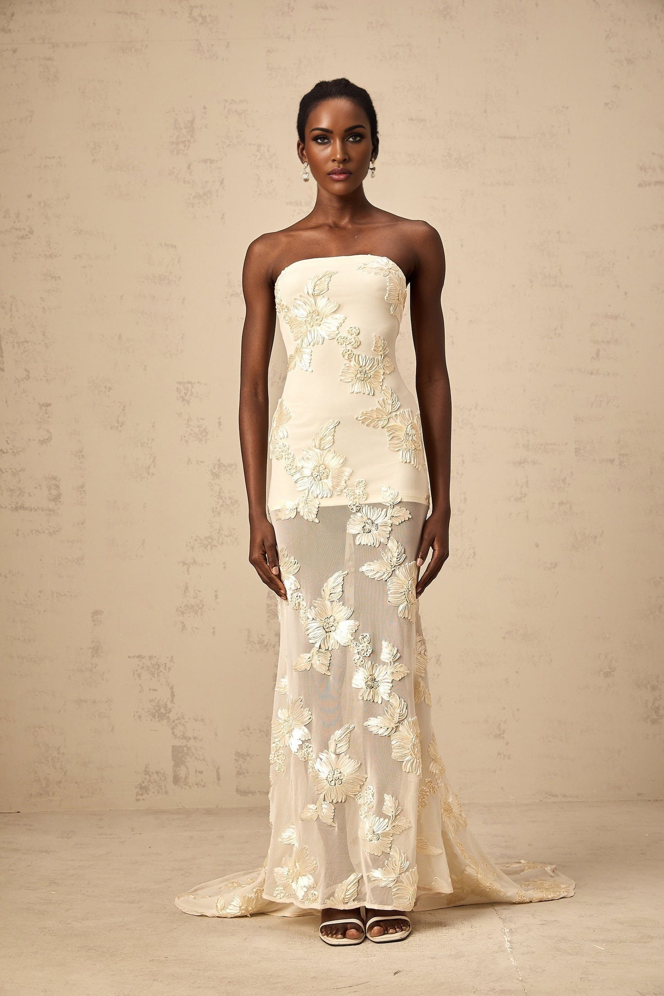 Woman wearing a neutral colored offshoulder maxi dress with embroidery details standing in a relaxed pose