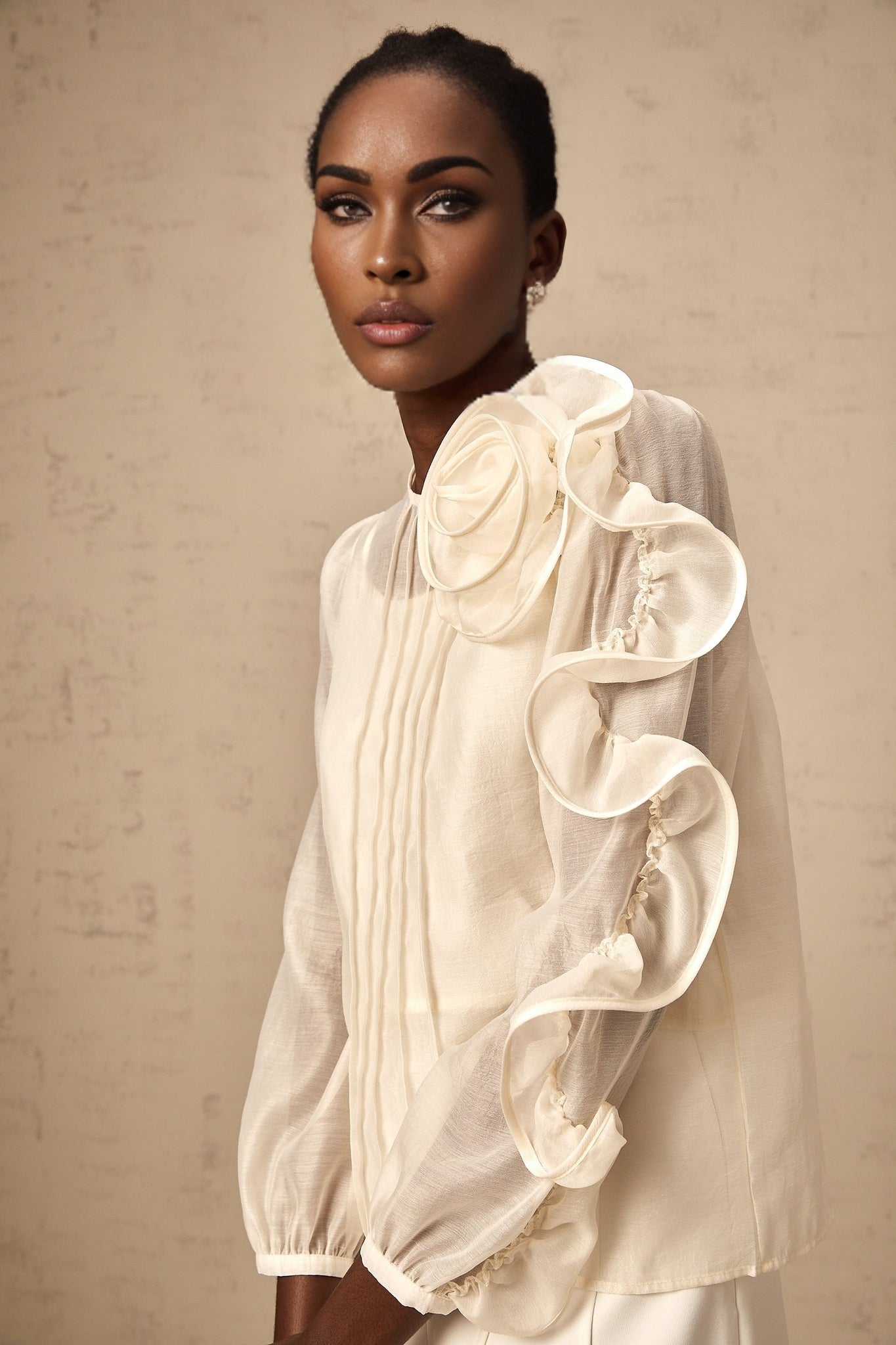 Woman wearing a neutral colored semi sheer blouse with 3d flower details