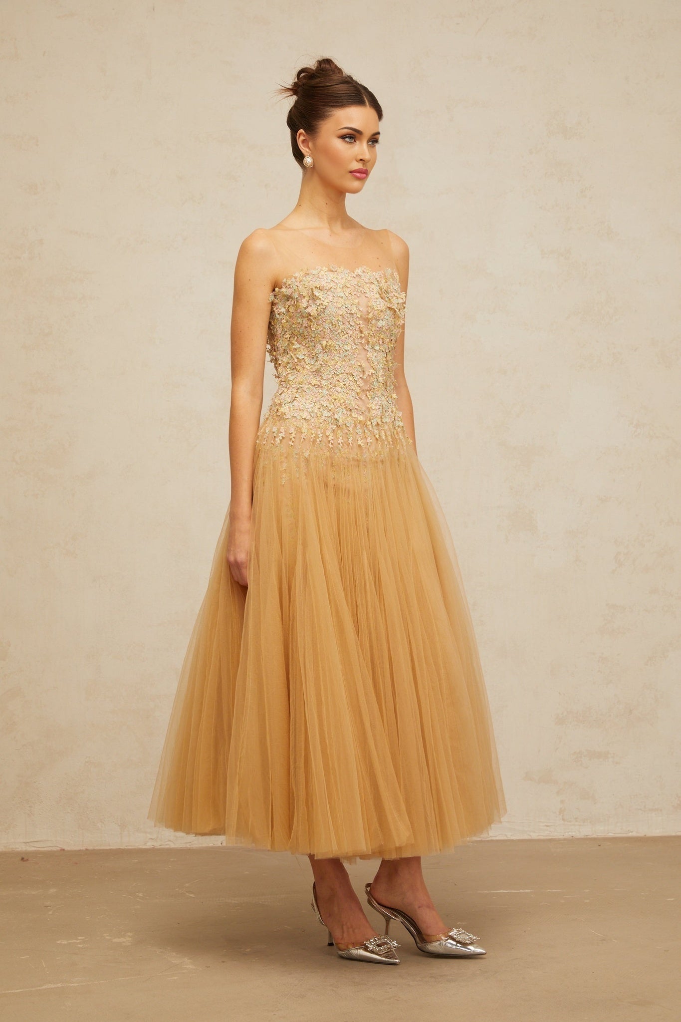 Woman wearing a neutral toned midi dress with pleated tulle and sequin embellishments