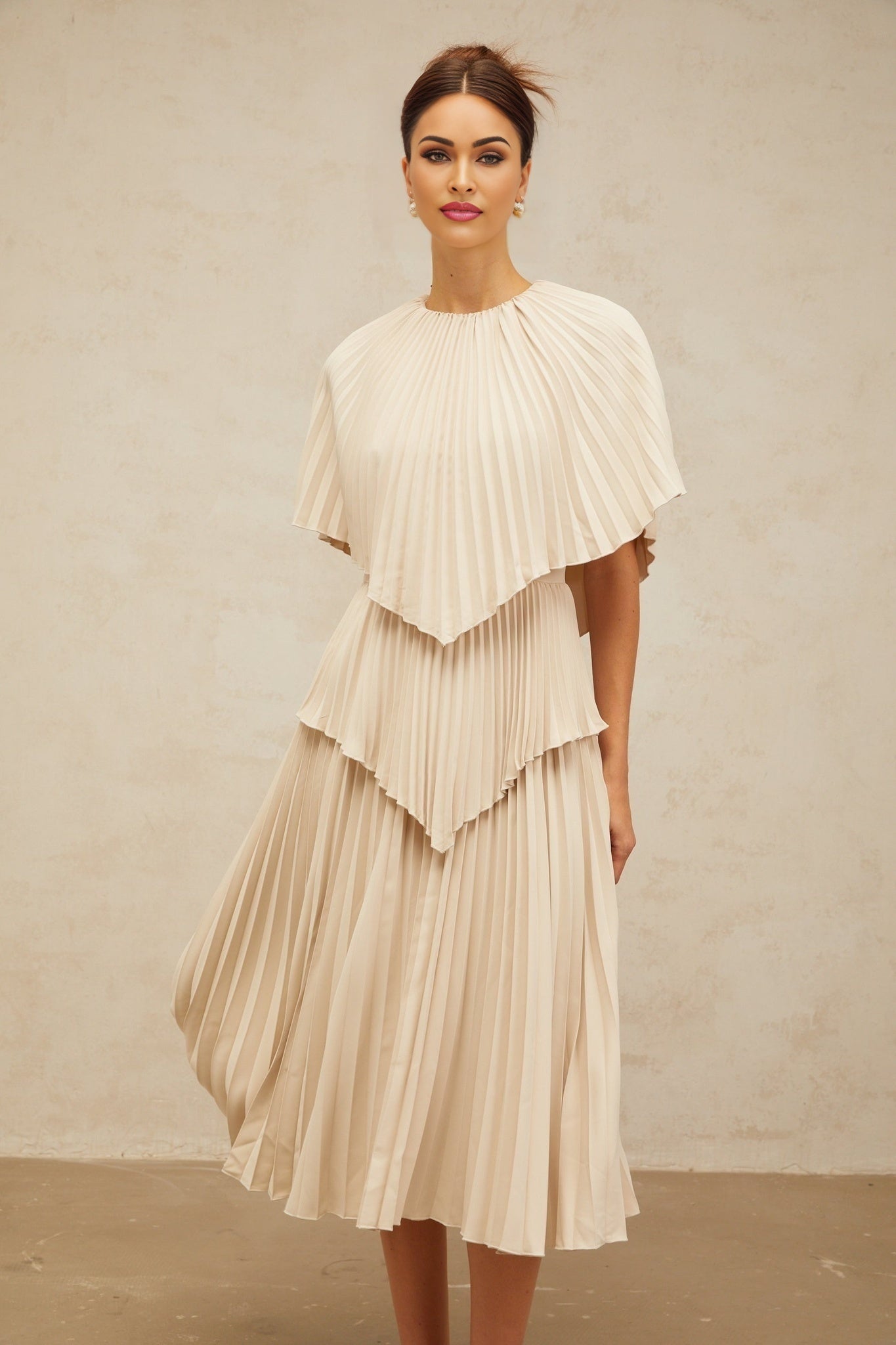 Woman wearing a neutralcolored capestyle pleated midi dress with flowing silhouette and elegant drape