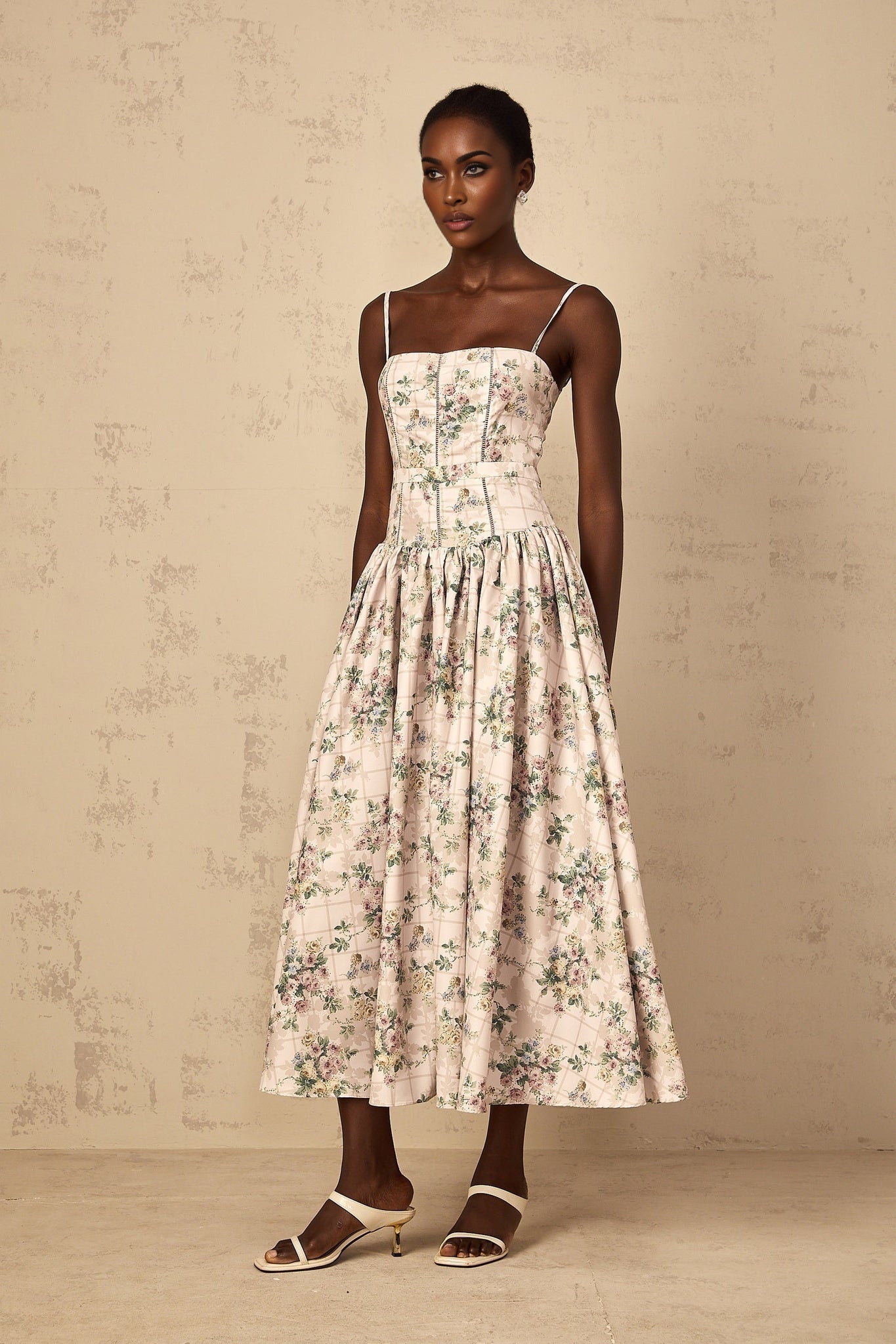 Woman wearing a neutralcolored midi dress with delicate floral print pattern standing in a relaxed pose
