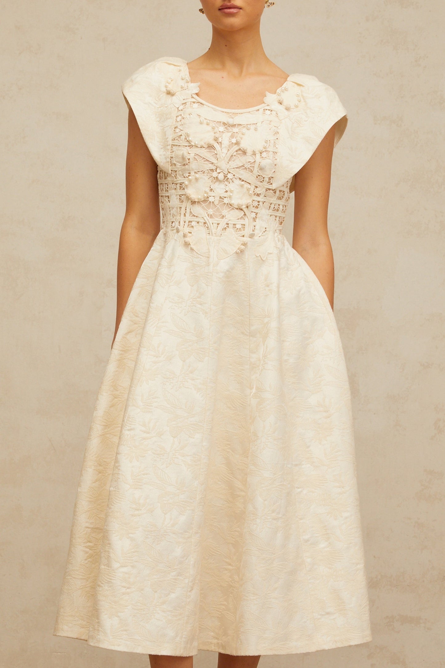 Woman wearing a neutralcolored midi dress with floral embroidery and embellishments