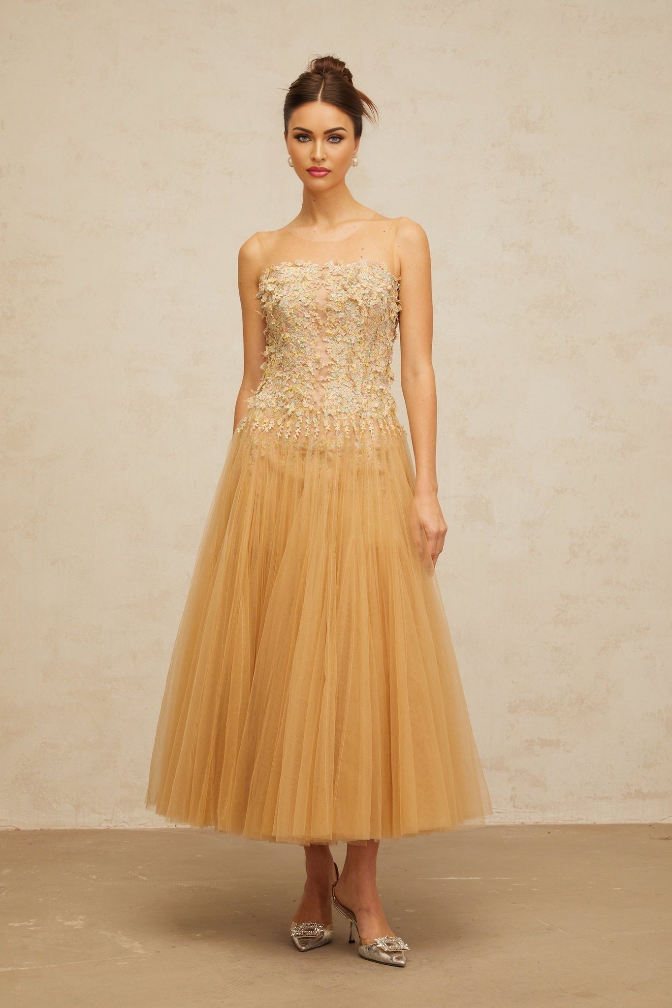 Woman wearing a neutralcolored midi dress with pleated tulle fabric and sequin embellishments