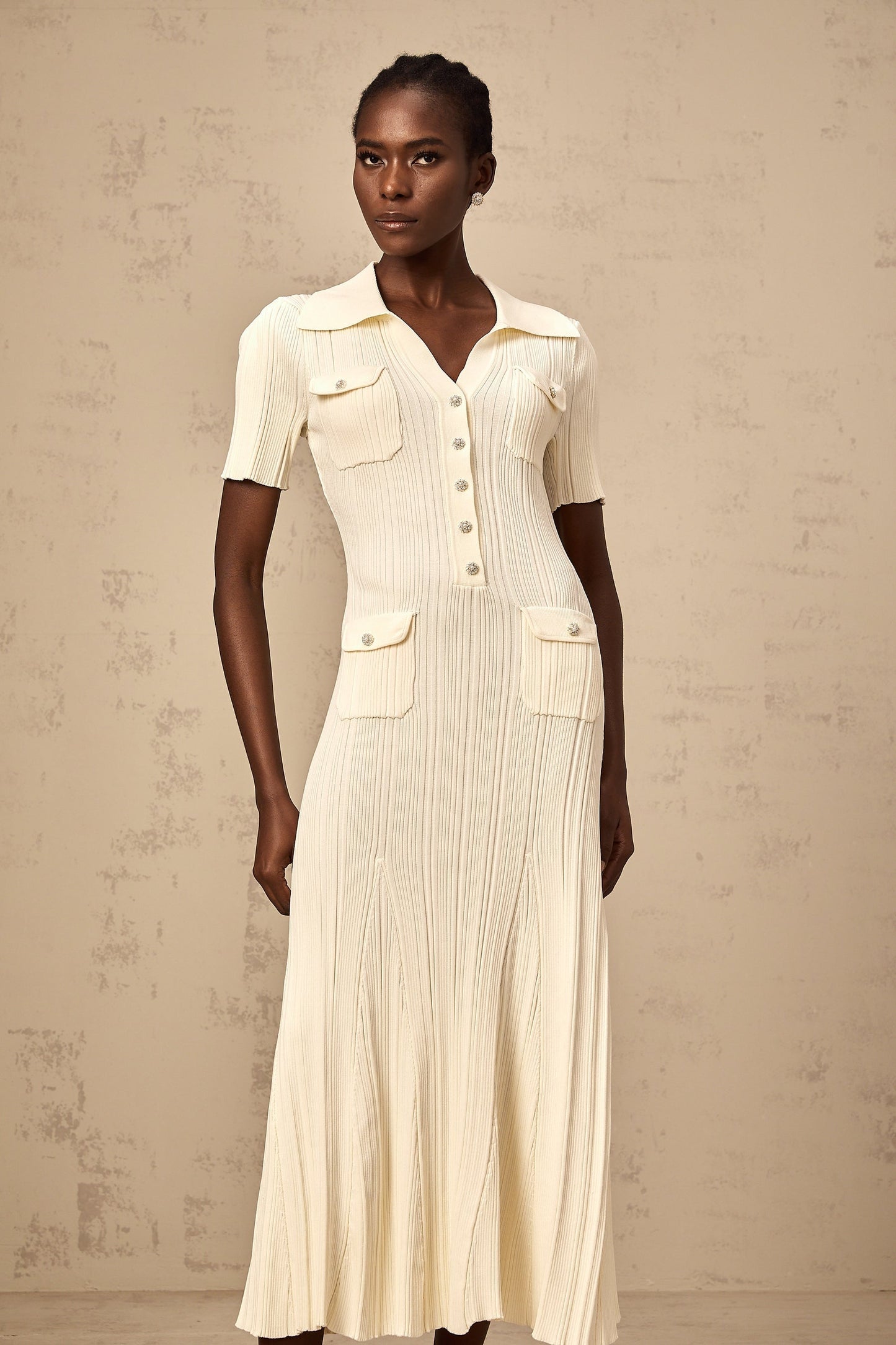 Woman wearing a neutralcolored ribbedknit midi dress with long sleeves standing against a plain background