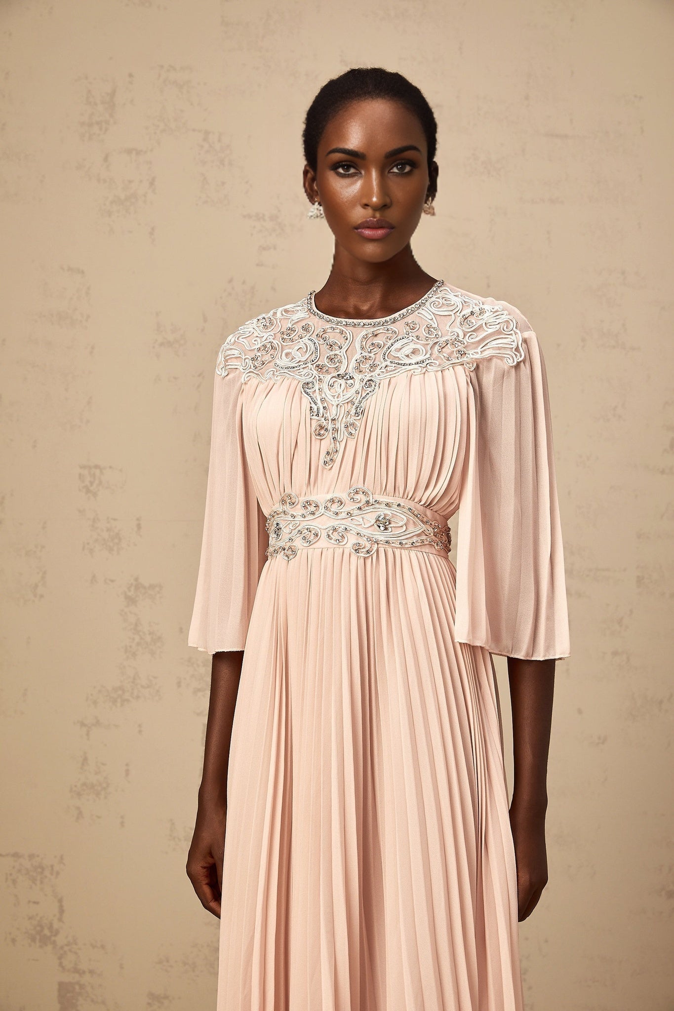 Woman wearing a pink crystal embellished midi dress with full pleats and sleeveless design