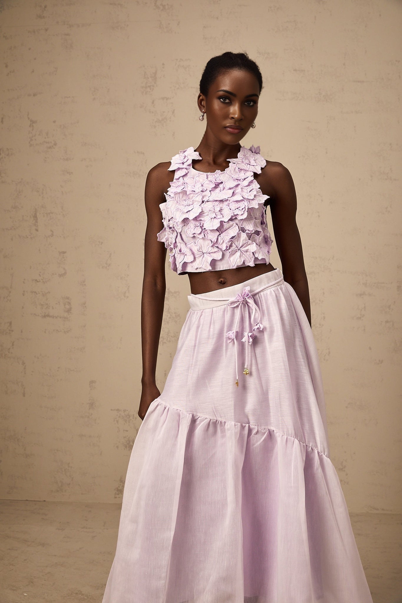 Woman wearing a purple matching set consisting of a sleeveless top and skirt adorned with faux flower details