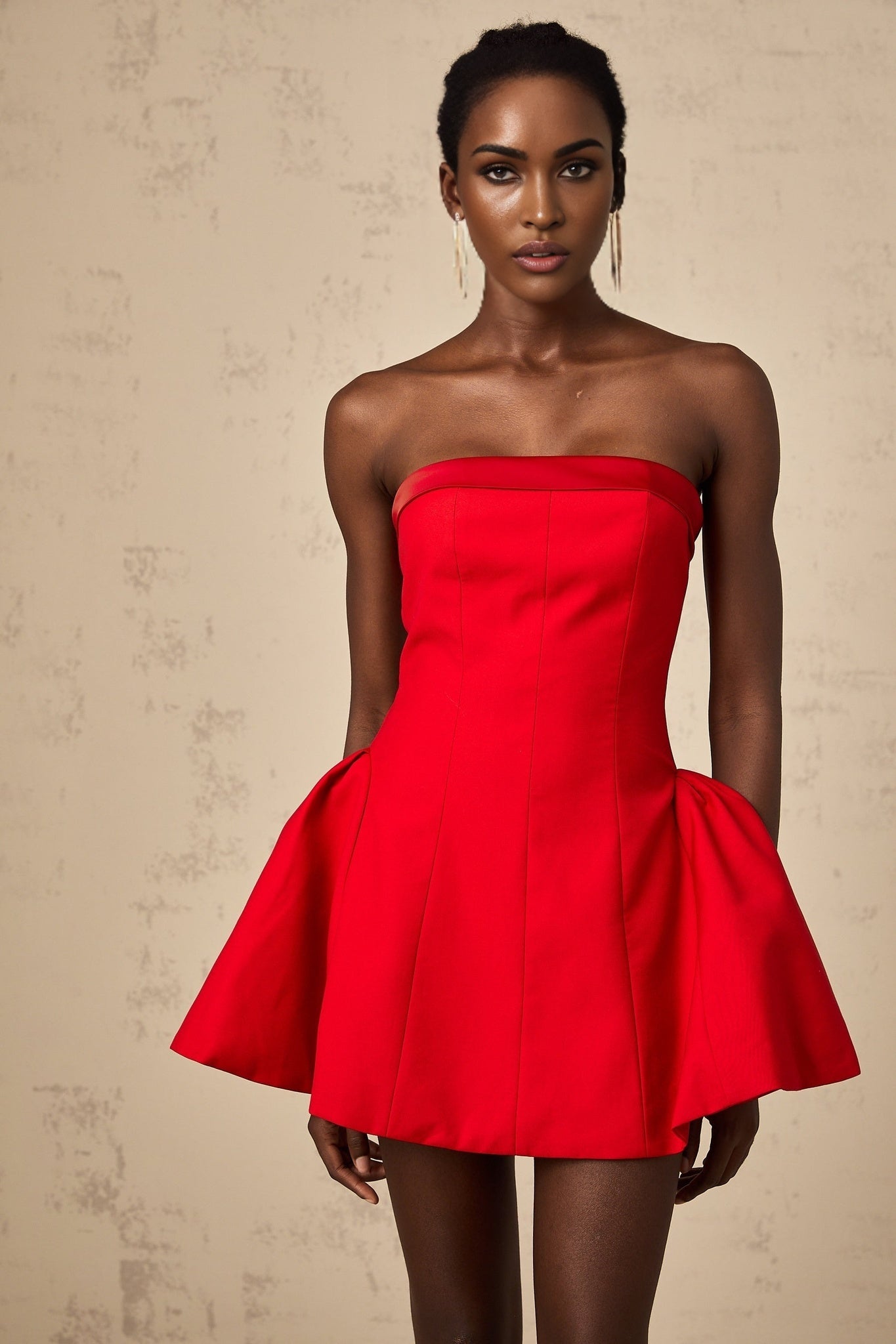 Woman wearing a red offshoulder mini dress with flared skirt standing against a plain background