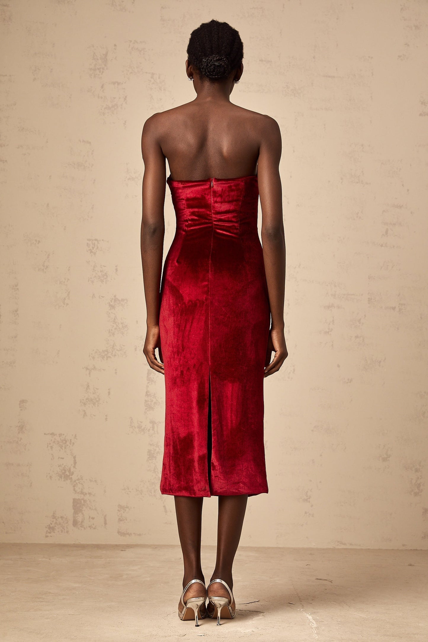 Woman wearing a red velvet midi dress with gathered details standing against a plain background