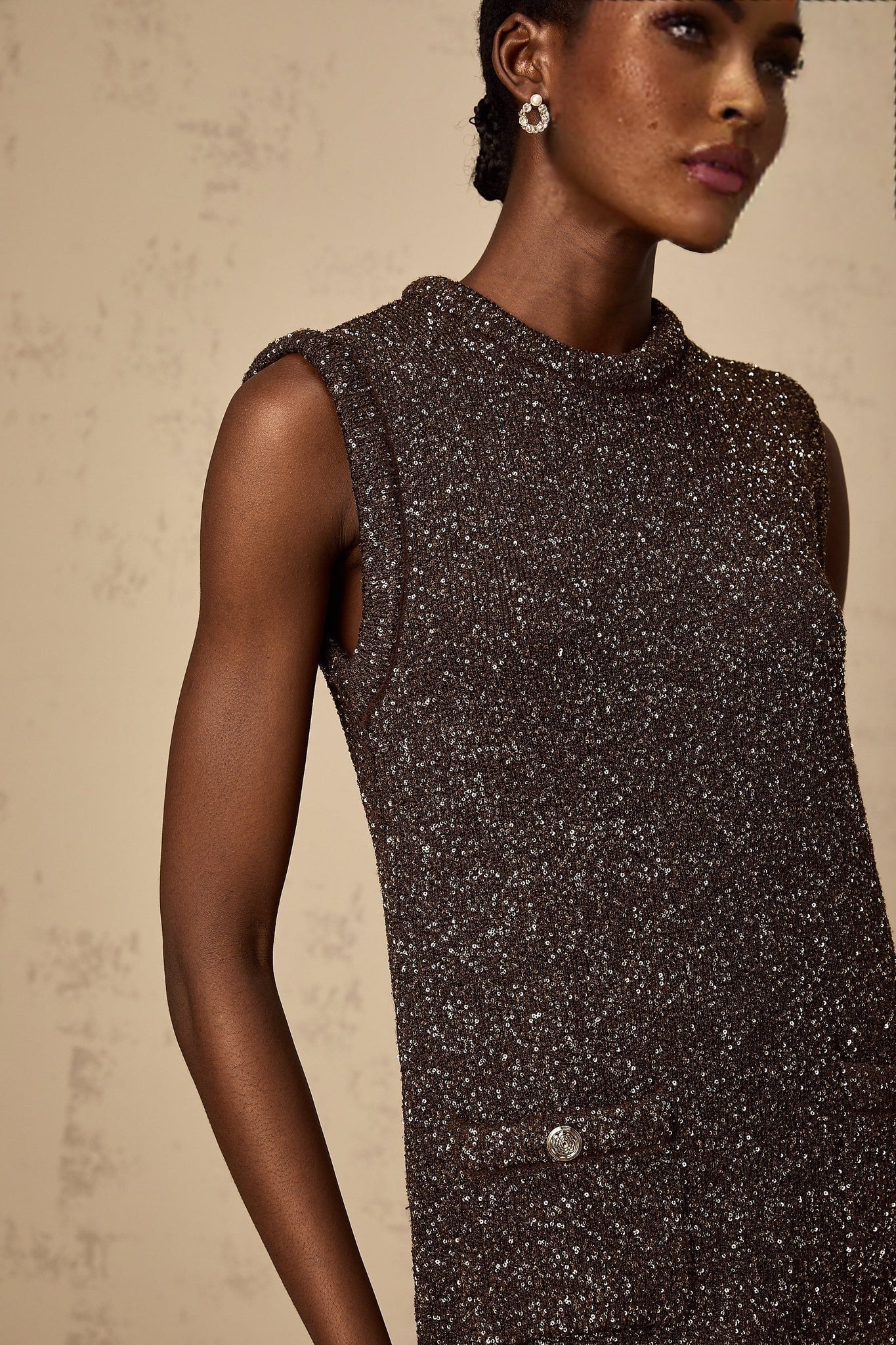 Woman wearing a short barley brown dress with sequin detailing and knit fabric standing against a plain background
