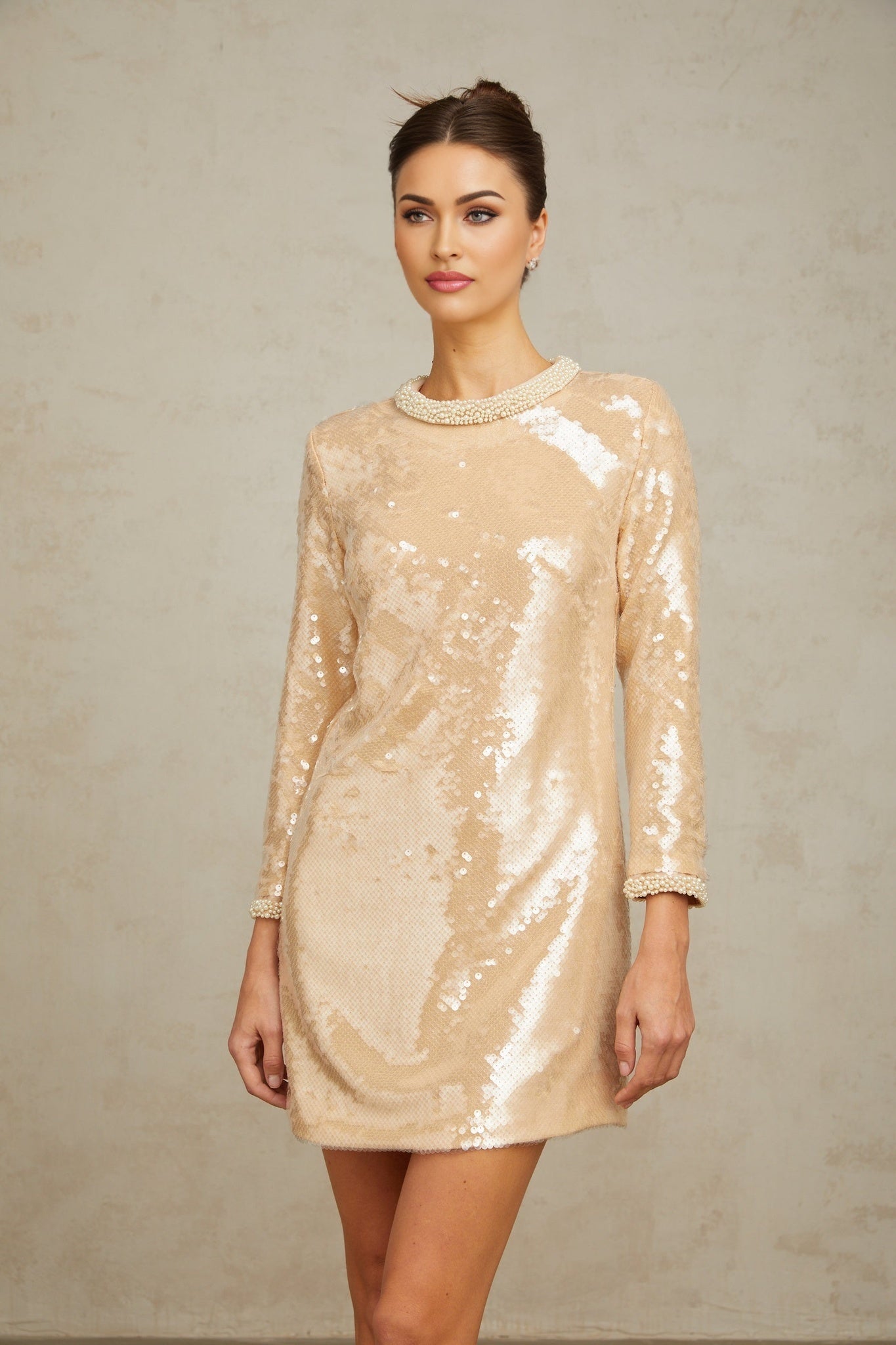 Woman wearing a short beige dress with faux pearl and sequin embellishments