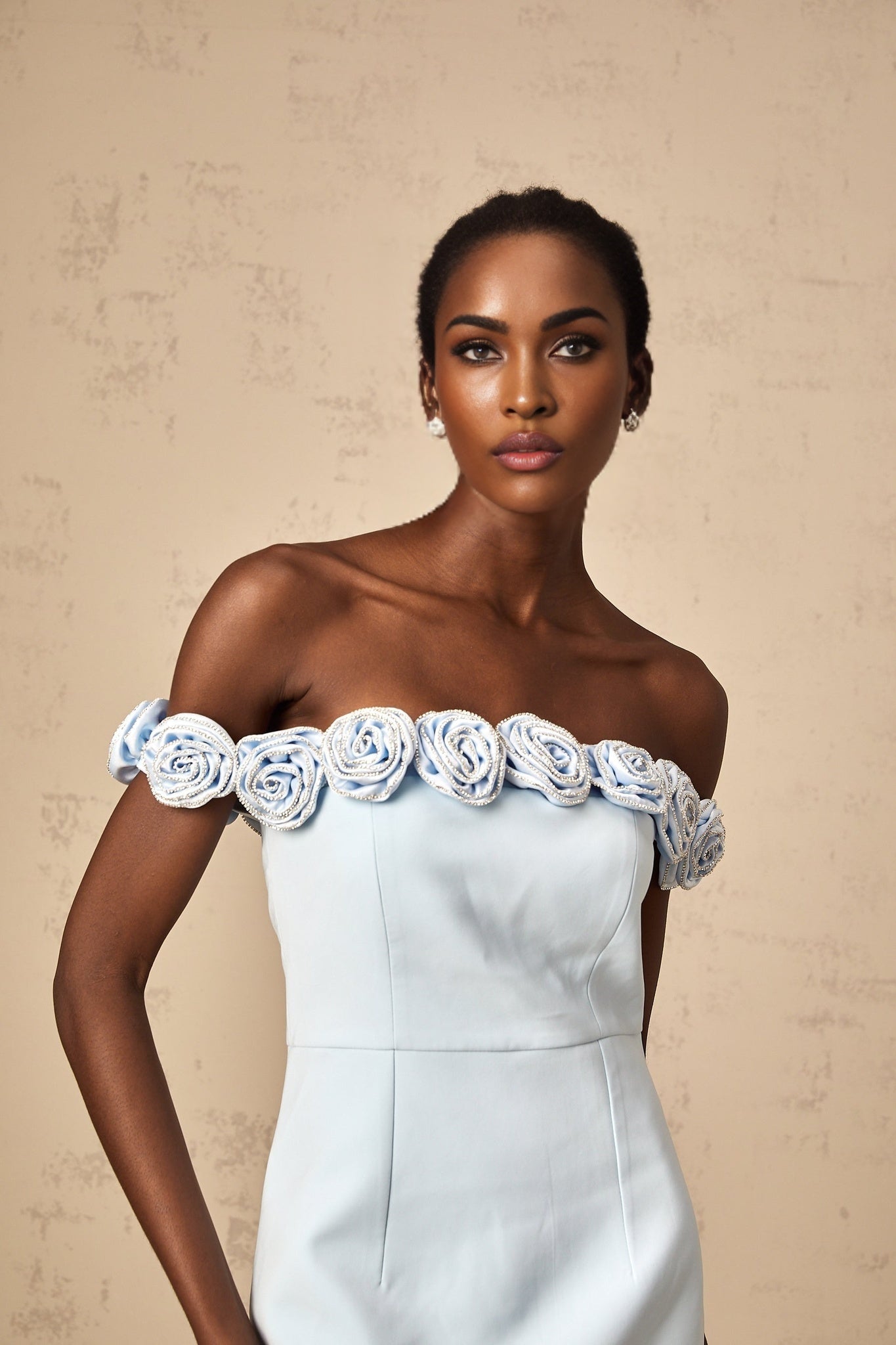 Woman wearing a short blue dress with floral applique details standing against a plain background