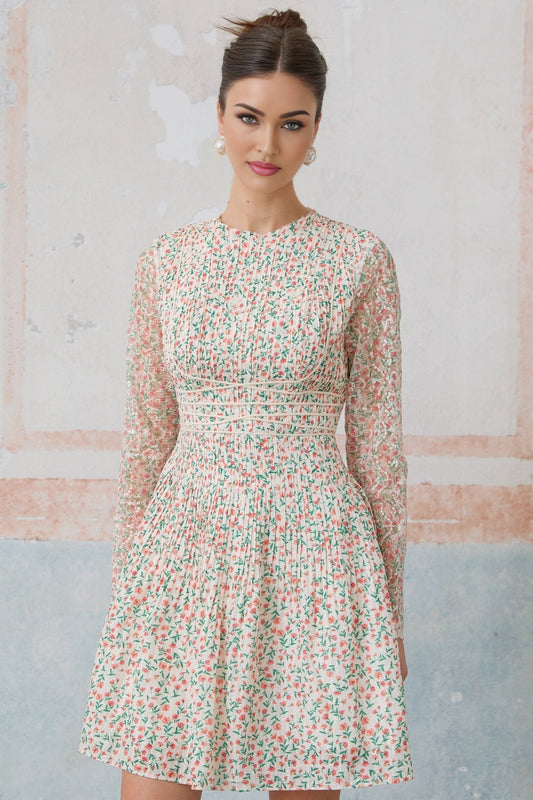 Woman wearing a short floral print dress with pleated skirt and Marion design standing in a neutral background