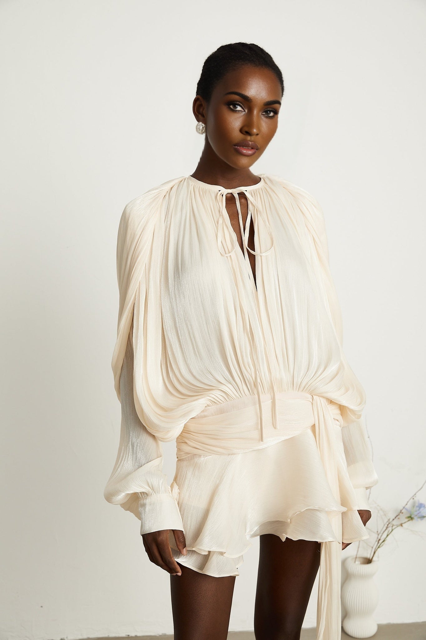 Woman wearing a short neutral colored pleated dress with ruffles and a flowy silhouette