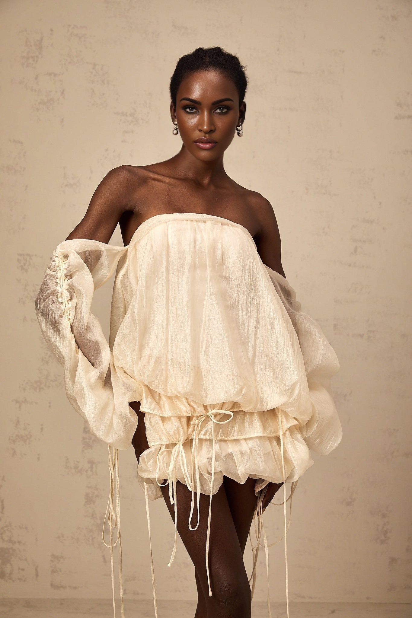Woman wearing a short offshoulder dress with ruched fabric and selftie details in a layered design