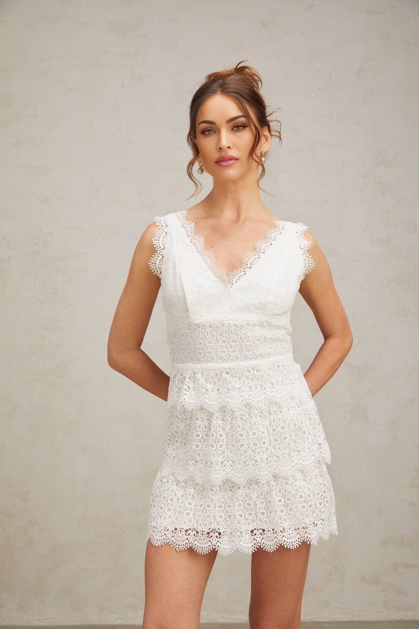 Woman wearing a short white lace dress with tiered skirt and delicate floral pattern