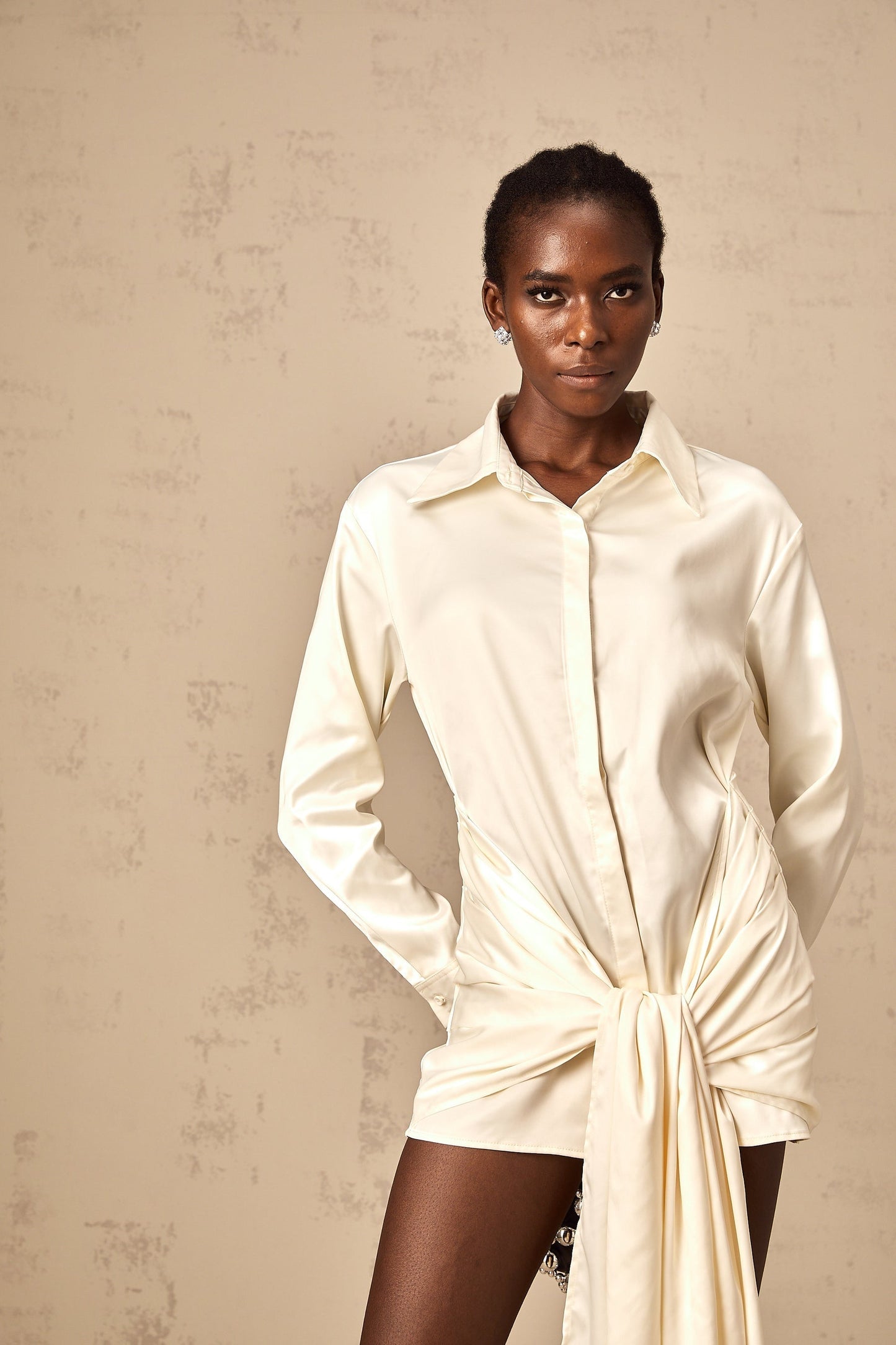 Woman wearing a short white shirt dress with ruched detailing and ribbon accents