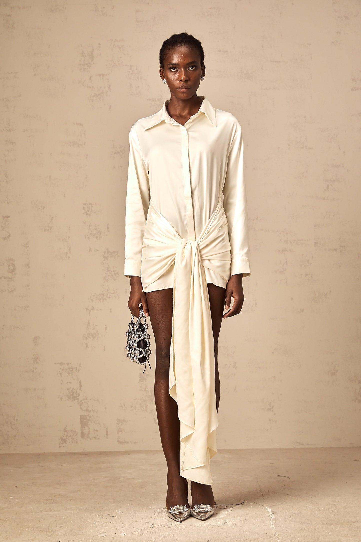 Woman wearing a short white shirt dress with ruched detailing and ribbon accents