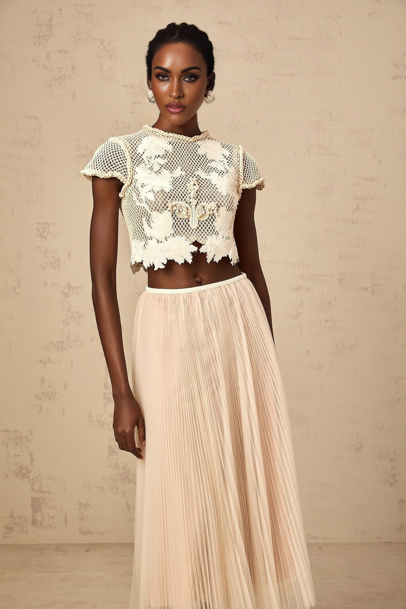 Woman wearing a twopiece outfit in neutral colors with floral applique details top and skirt set
