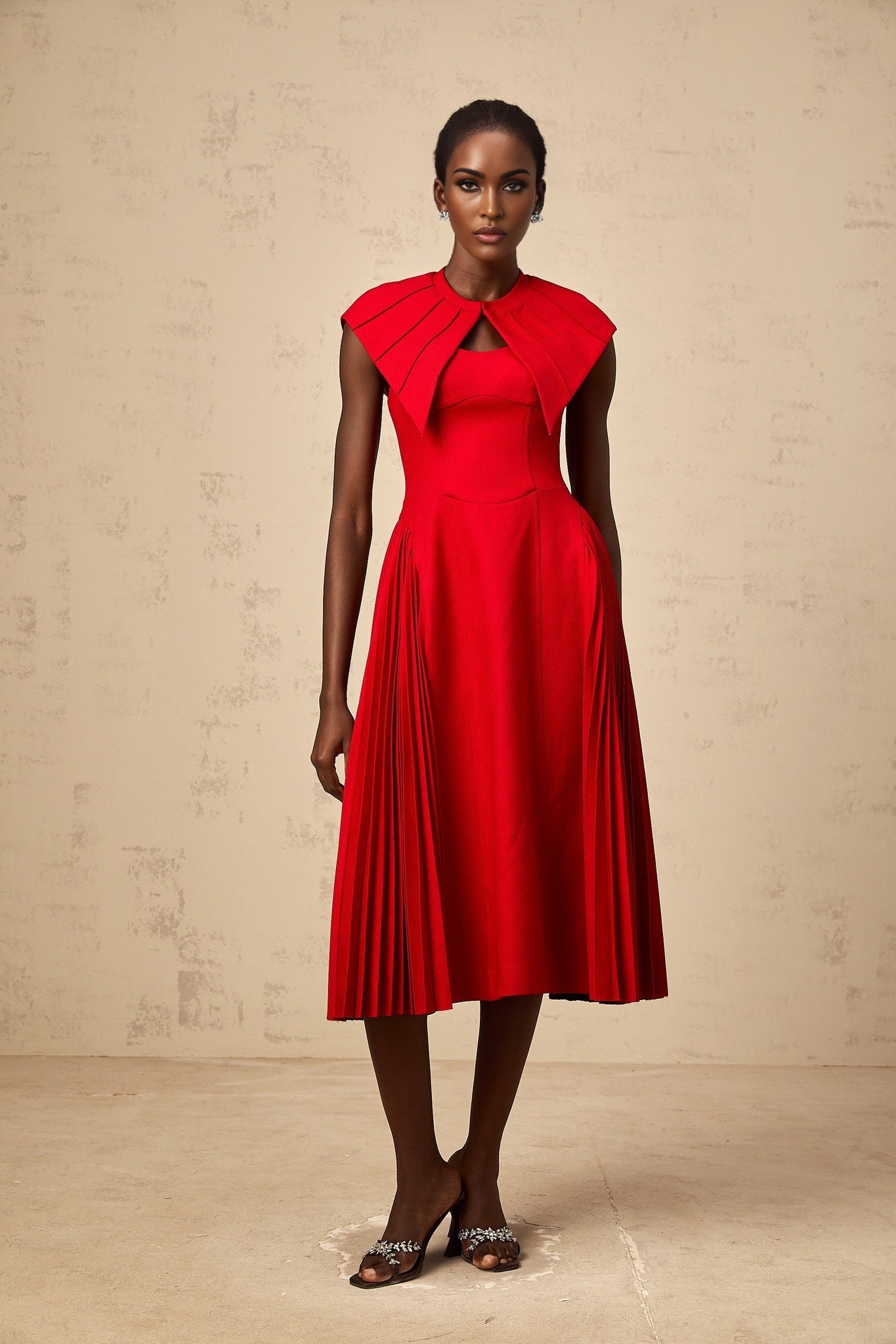 Woman wearing a vibrant red midi dress with capelike details and pleated skirt