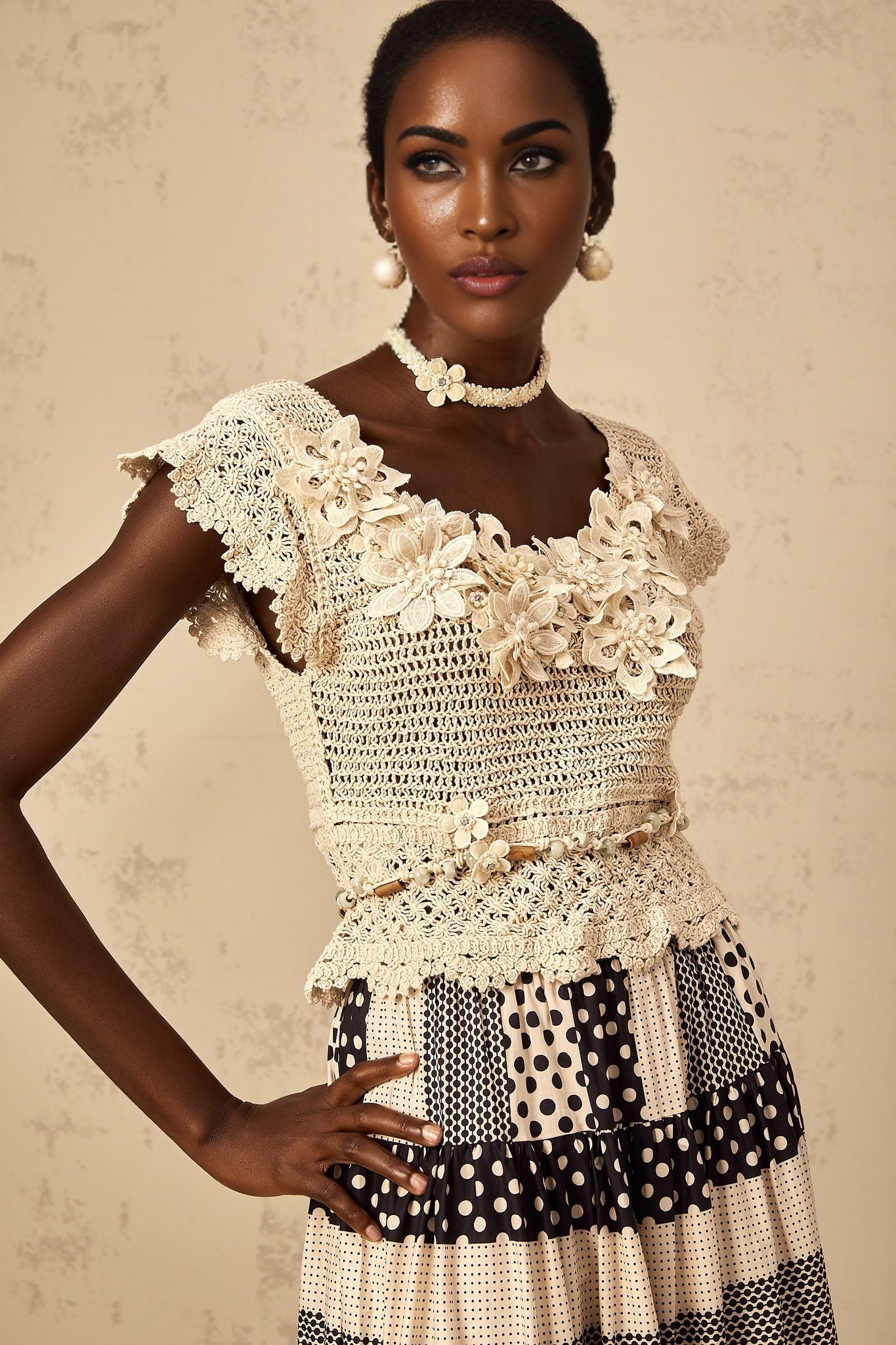 Woman wearing a white crochet knit top with 3D floral petal beading detail and short sleeves