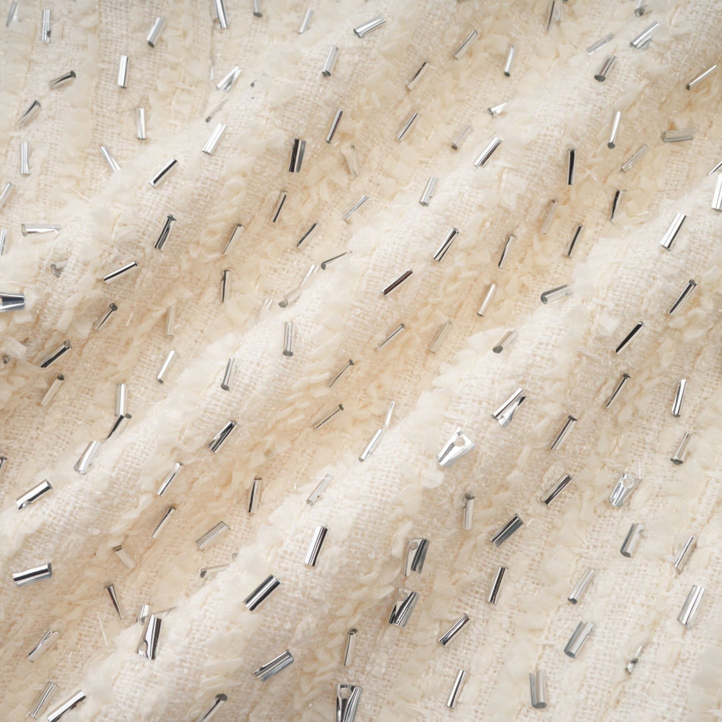 Woman wearing a white cropped jacket with beaded details and ruffle accents on a plain background