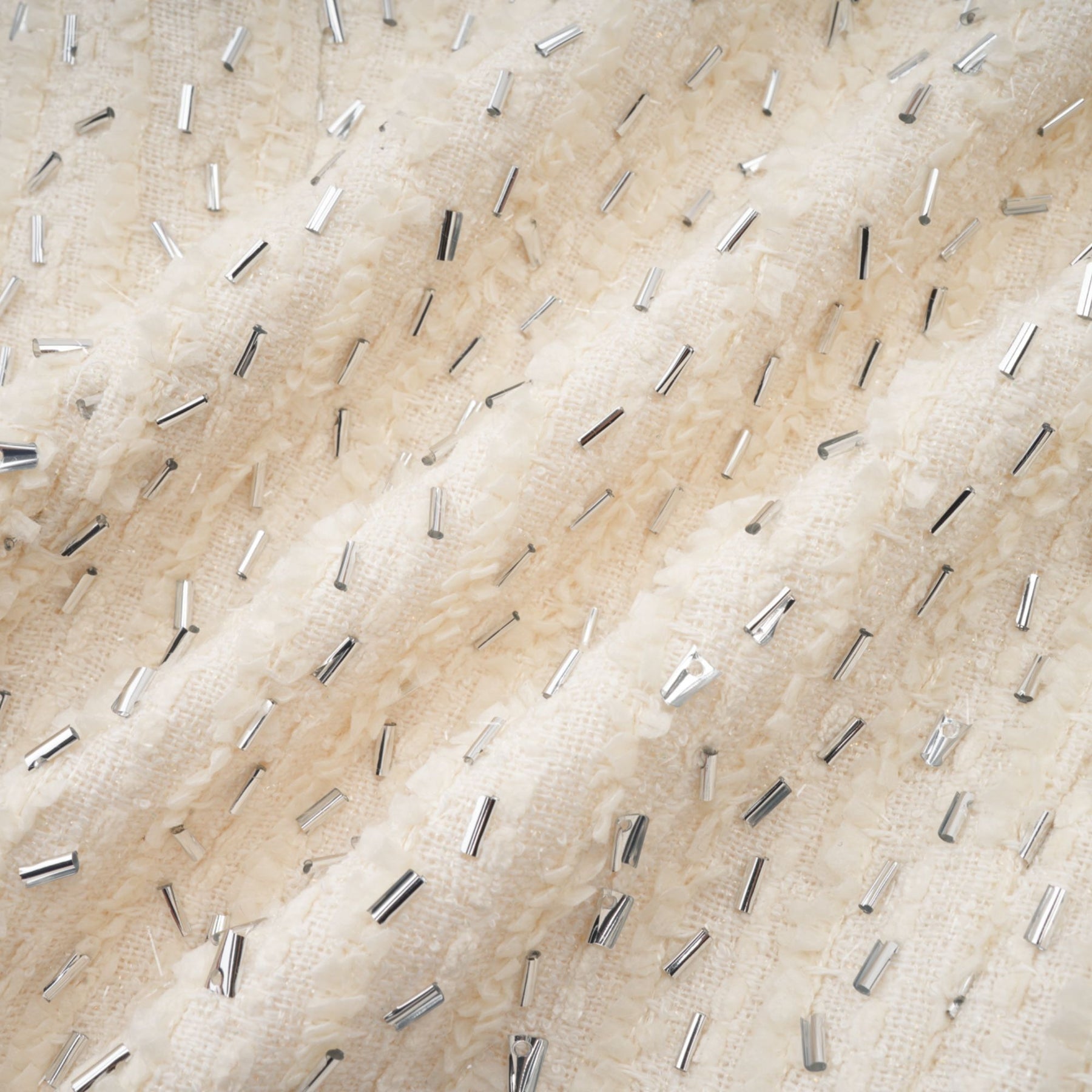 Woman wearing a white cropped jacket with beaded details and ruffle accents on a plain background