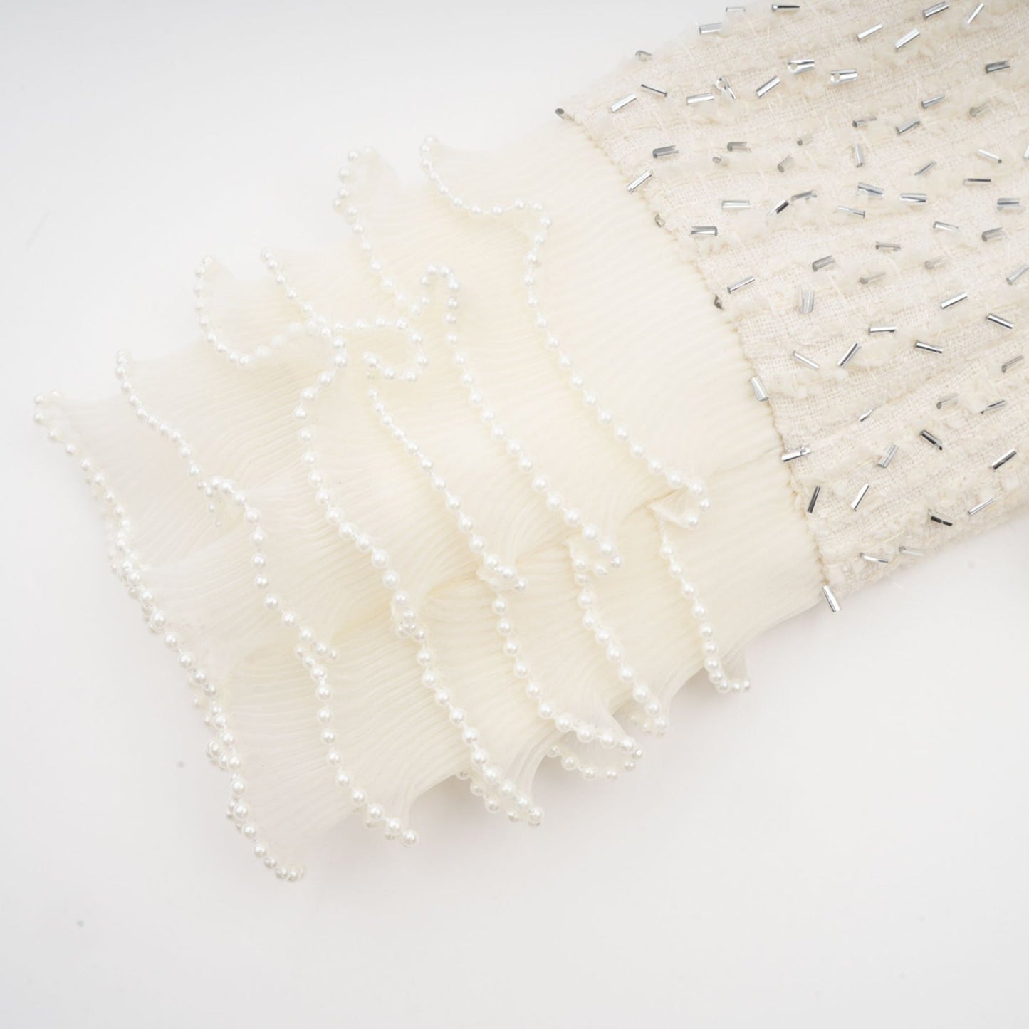 Woman wearing a white cropped jacket with beaded embellishments and ruffle details on a plain background