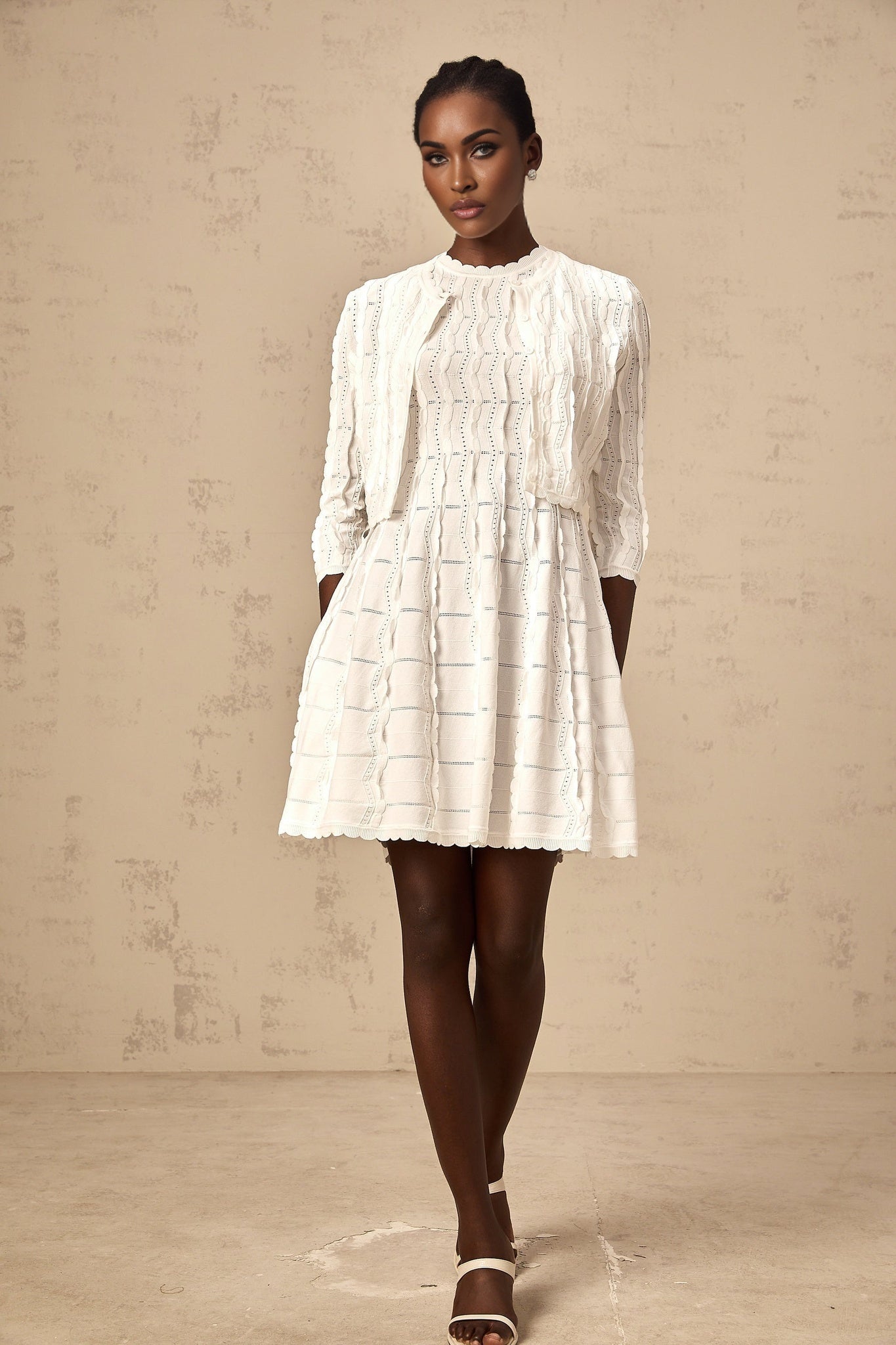 Woman wearing a white knitted cardigan with ruffled details and long sleeves