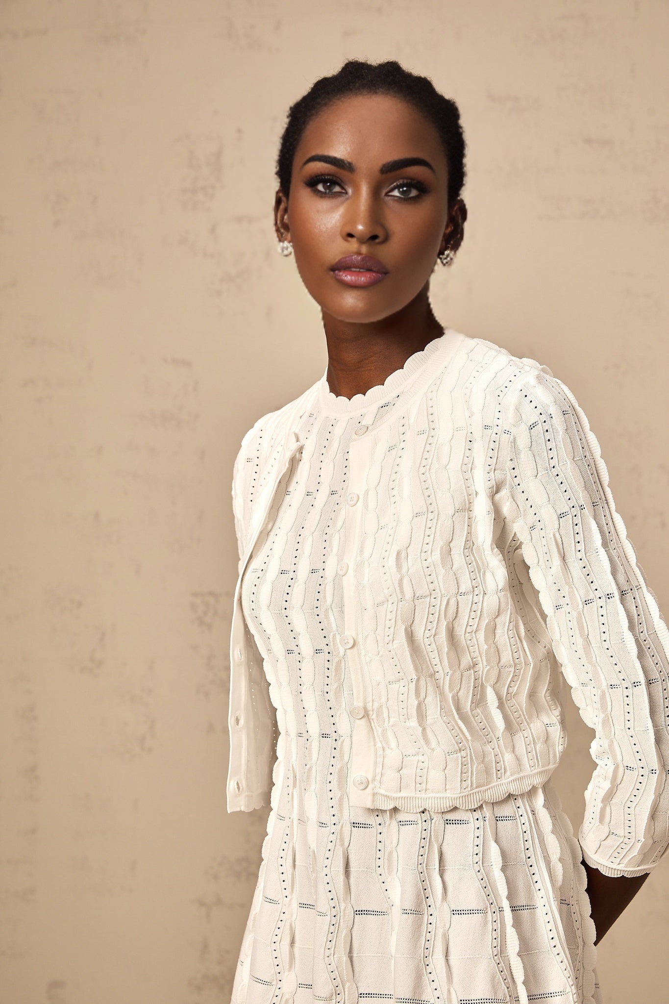 Woman wearing a white knitted cardigan with ruffled details and long sleeves